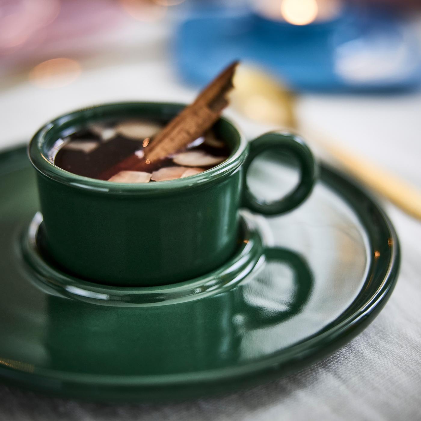 Close-up of green cup with saucer, filled with mulled wine and a vanilla stick.