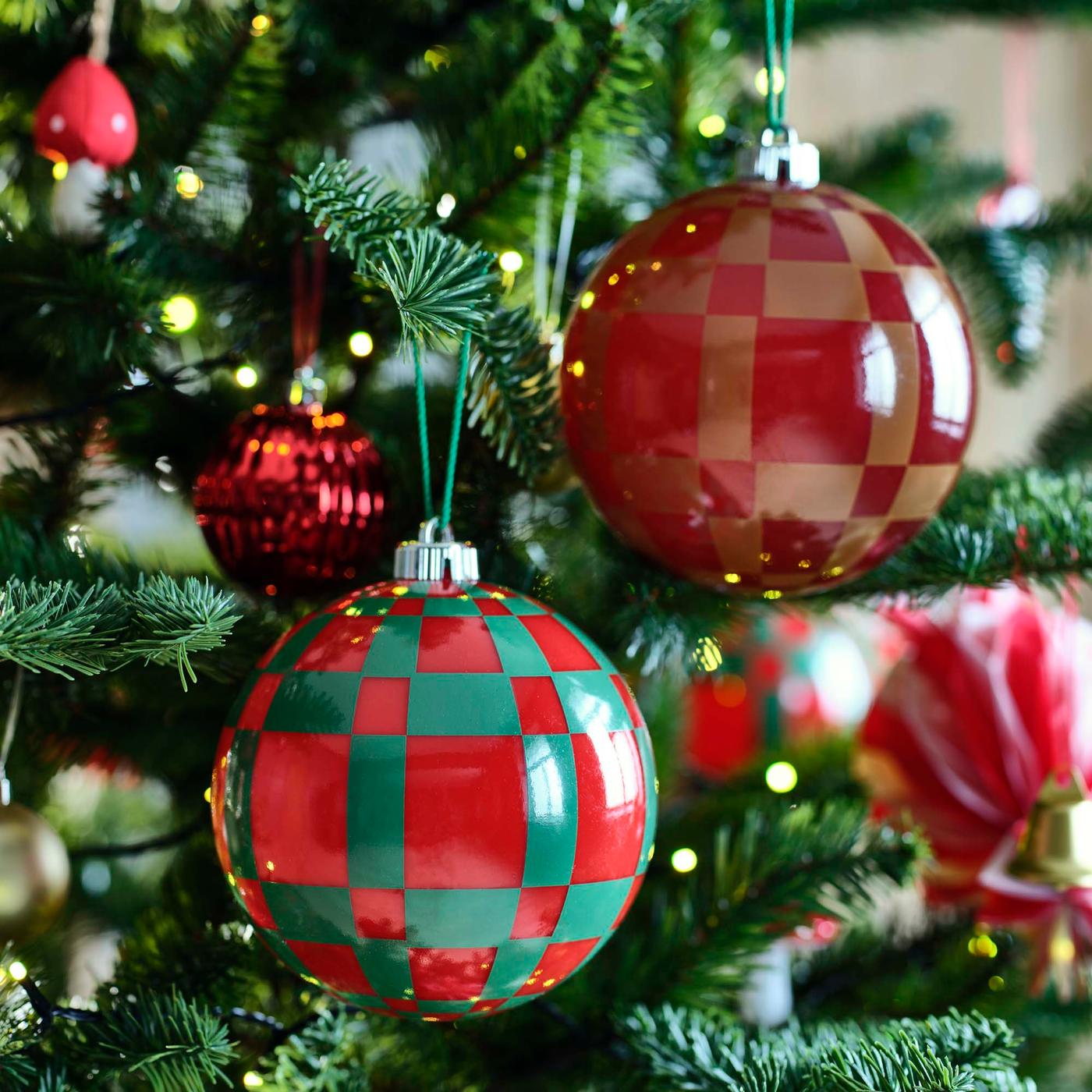 A close-up of large red and green baubles hanging on a Christmas tree.