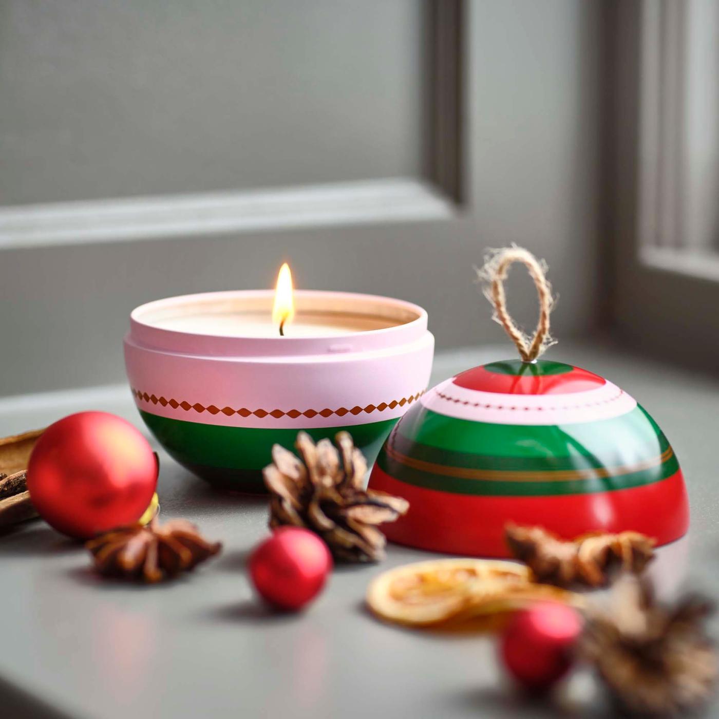 A close-up of a pink, green and red striped candle shaped like a Christmas bauble.