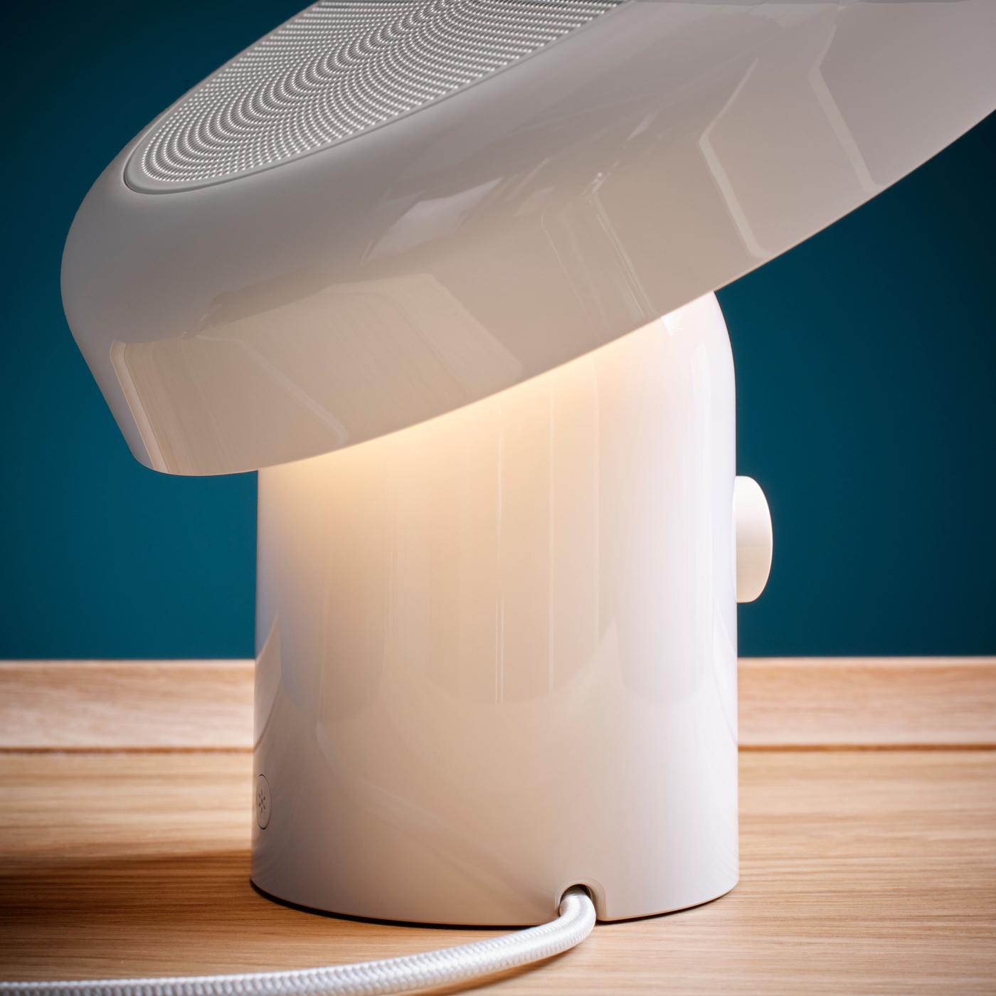 A close-up of a white speaker lamp with soft, warm light shining downward.