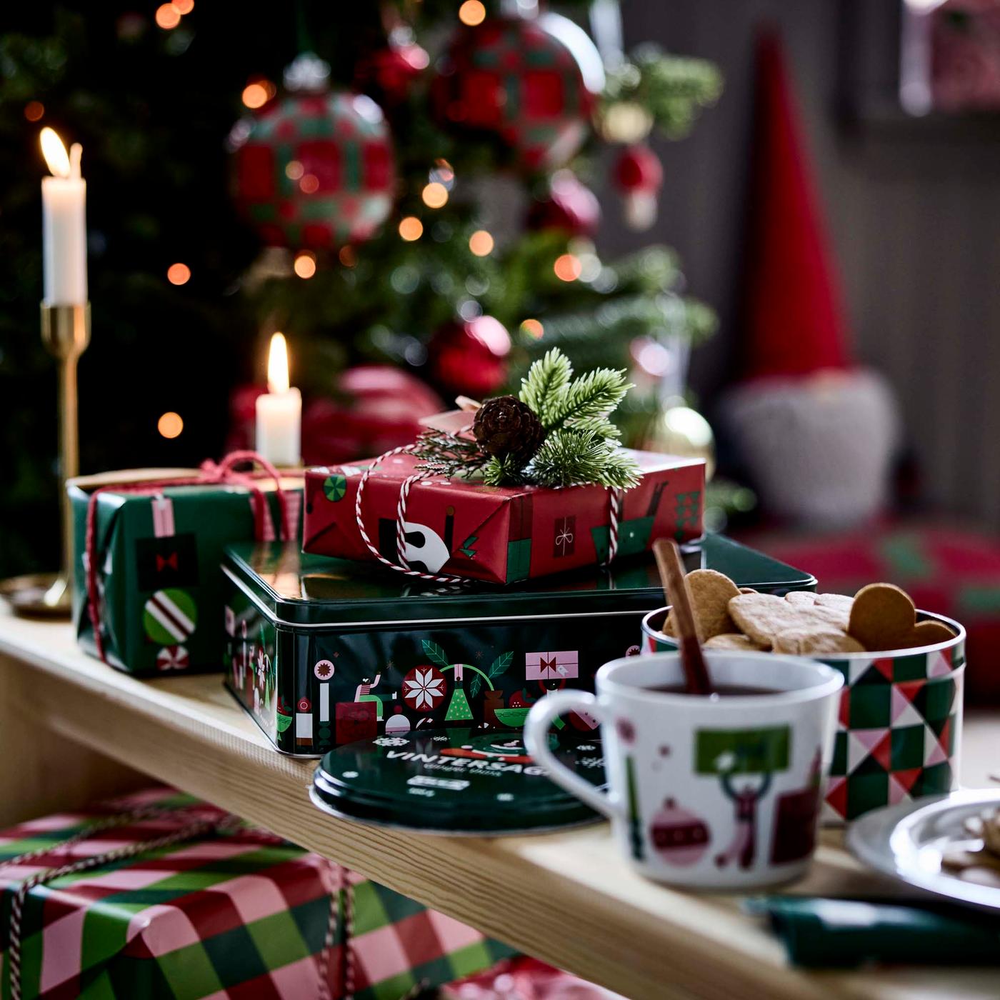 A close-up of Christmas gifts wrapped in green and red patterned paper beside festive mugs.