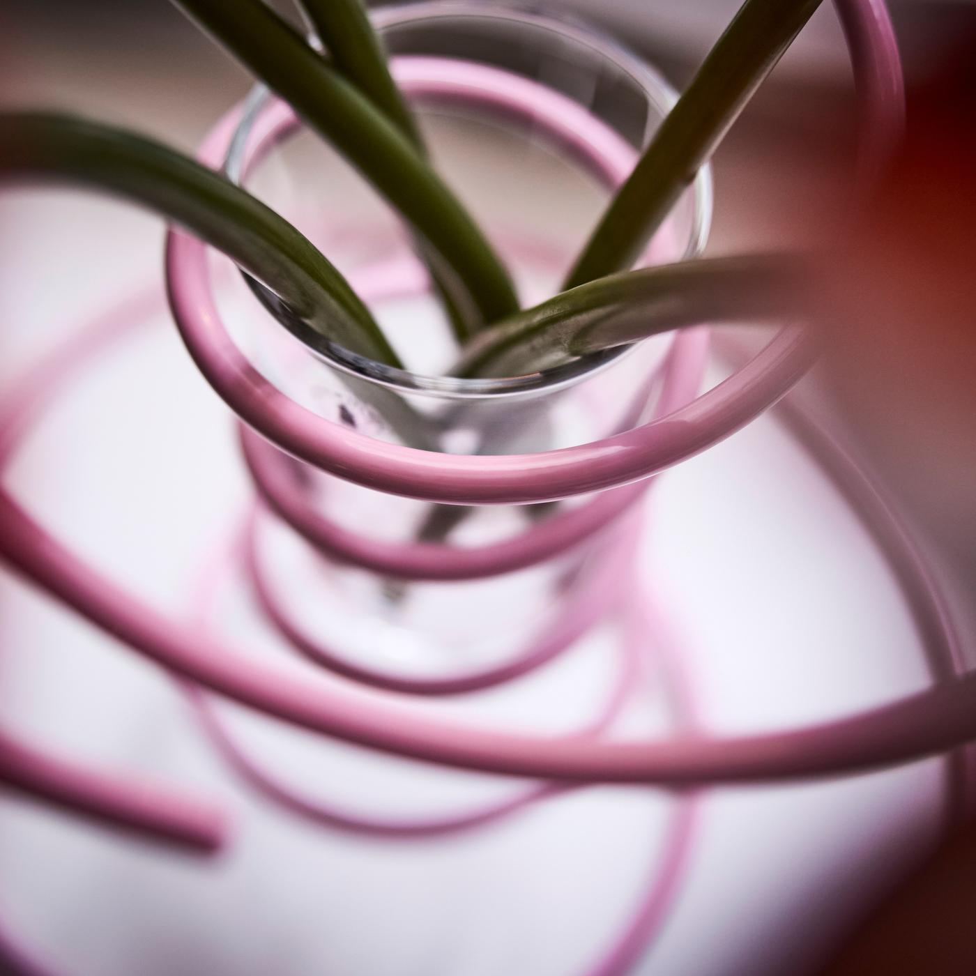 Close-up of a pink spiral-shaped steel vase seen from above, showing stems of flowers inside.