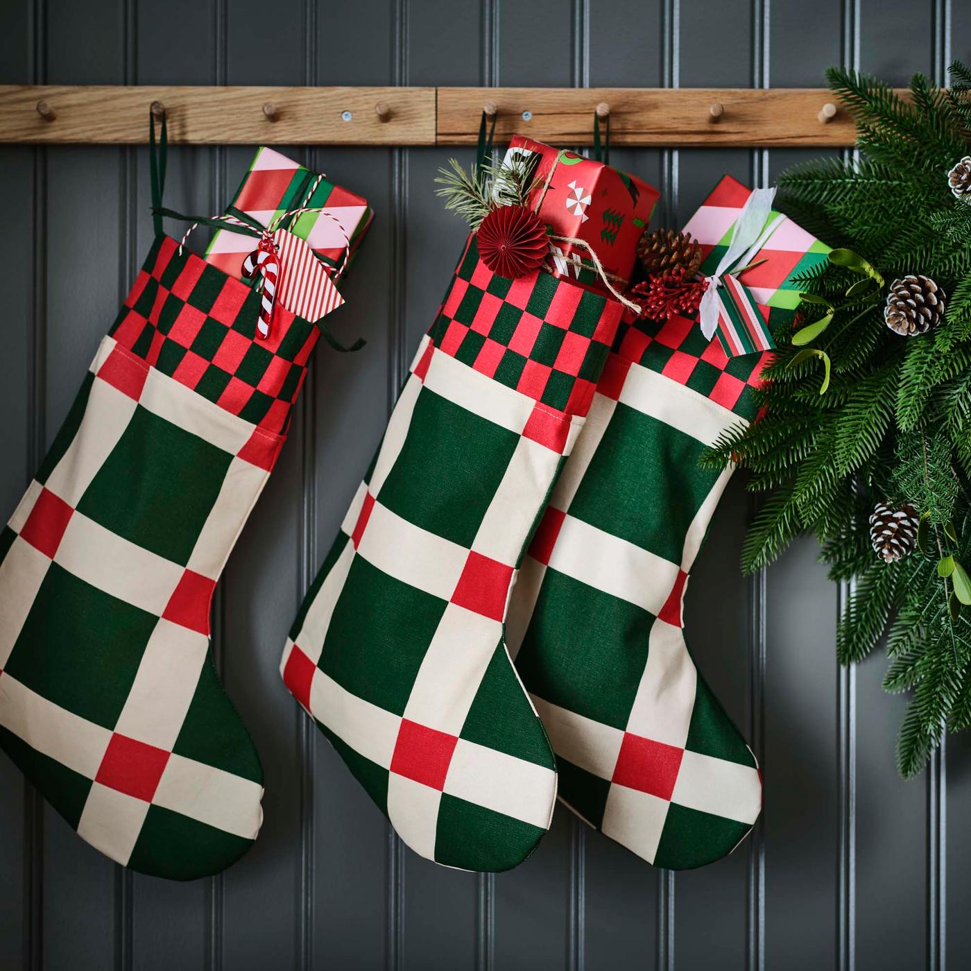 Three Christmas stockings with a red, green and white graphic design hanging from wooden hooks.