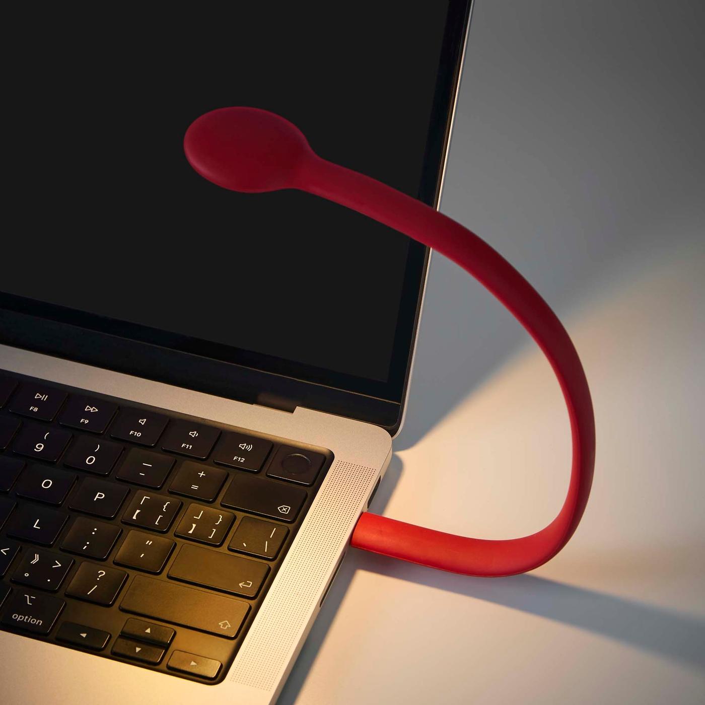 A small curved red lamp attached to a laptop lights up the keyboard.