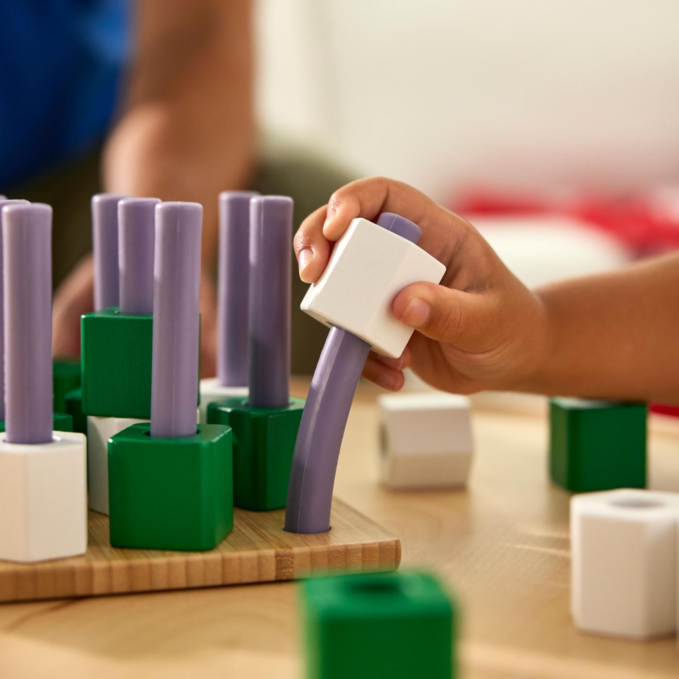 Green building blocks stacked on a white surface with hands assembling them.