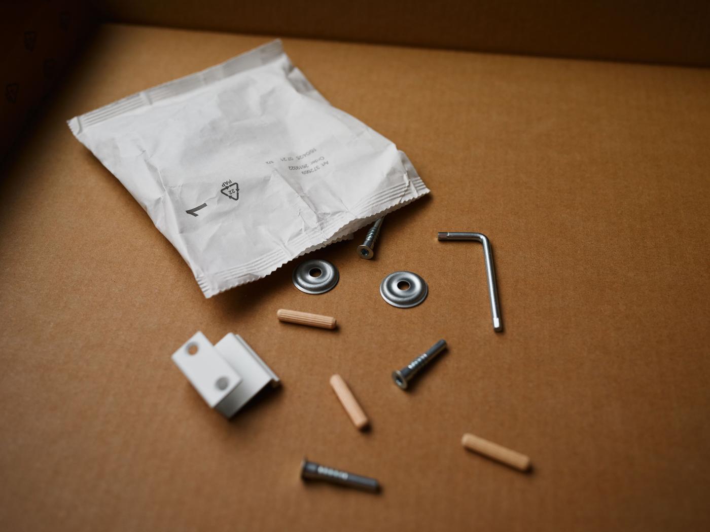 A paper-based fitting bag cut open on a table, with nuts, bolts, allen keys and plugs lying around.
