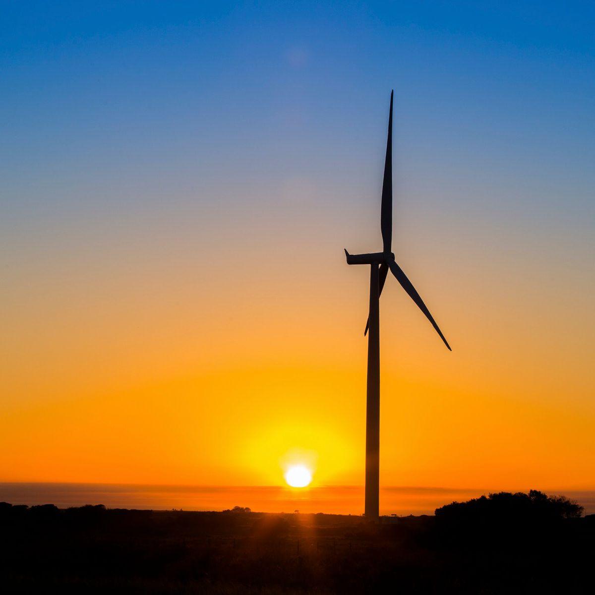 A wind turbin with the sun setting in the background.