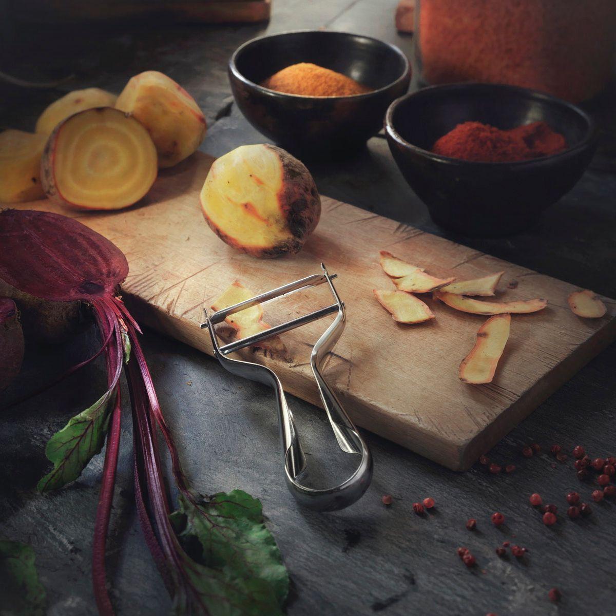 A cutting board, a potato peeler and vegetables.
