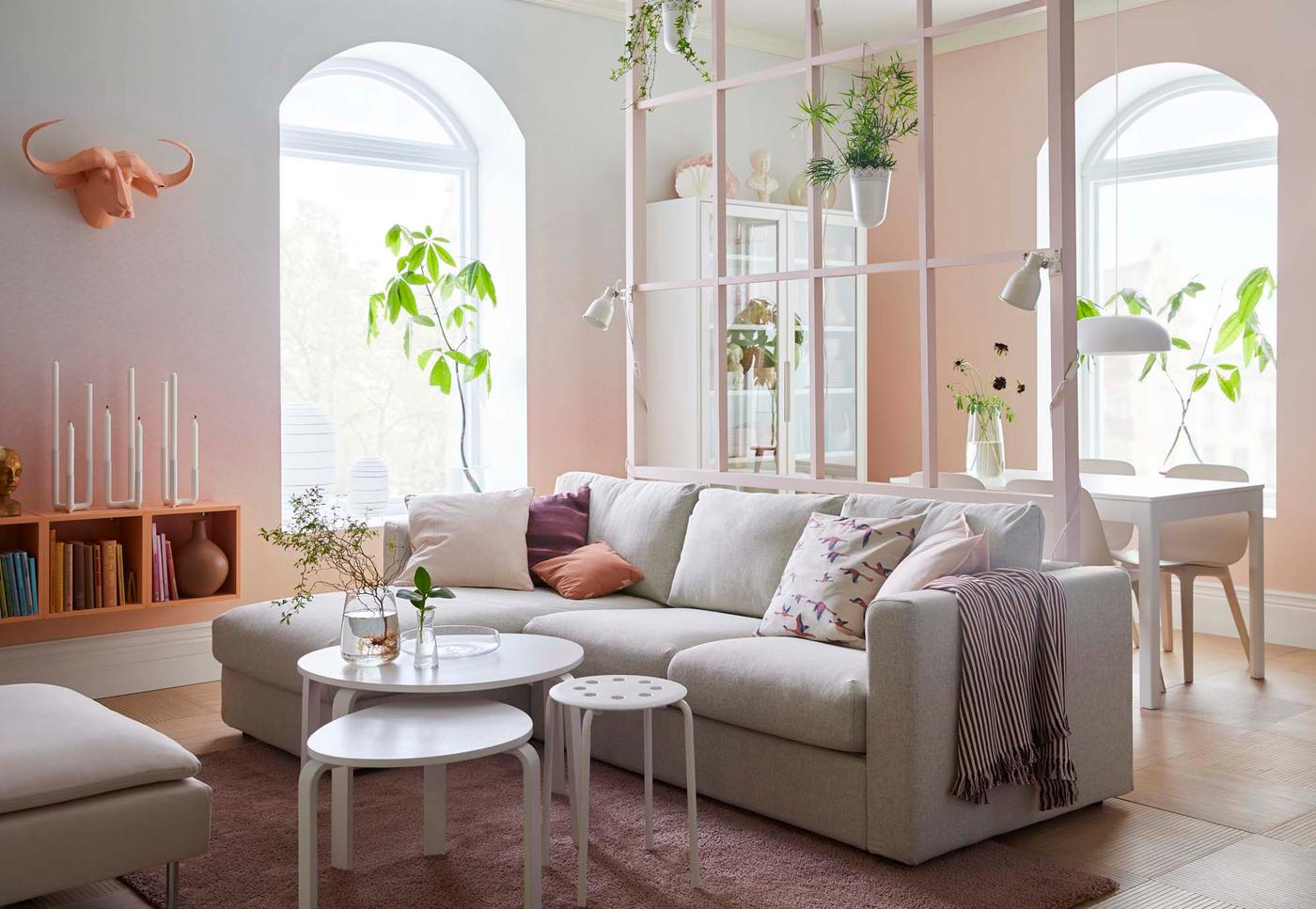 A bright living/dining room with two arched windows in the background. In the foreground is a grey sofa and a nest of three grey tables.