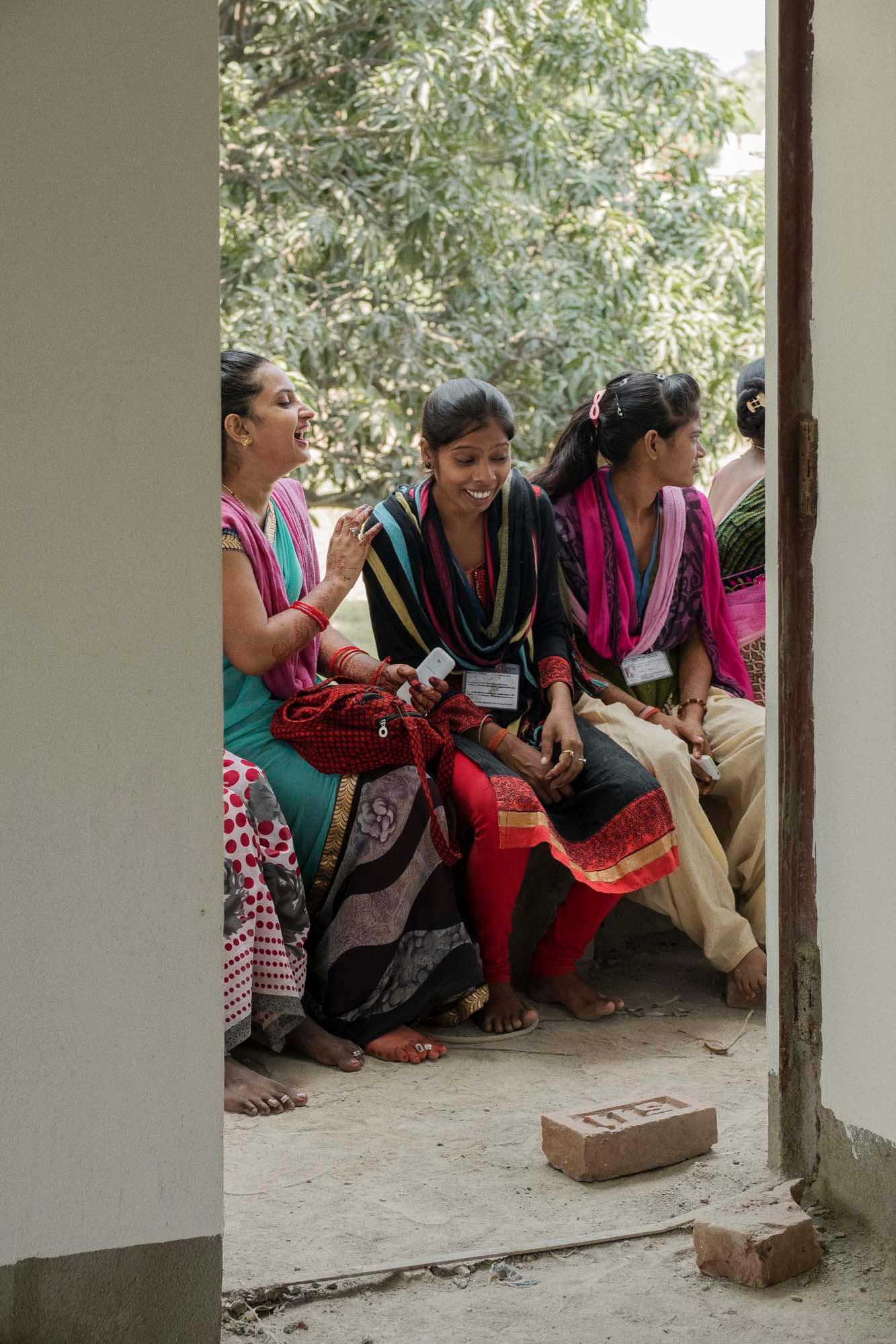 A group of women, seen through a doorway. They are sitting closely together on a bench, talking and laughing.