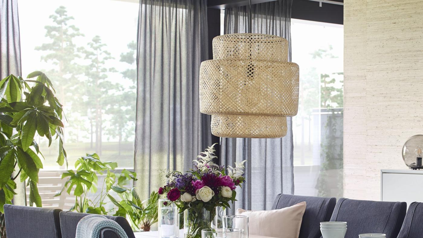 A SINNERLIG pendant lamp hanging from the ceiling in a light room with large windows.