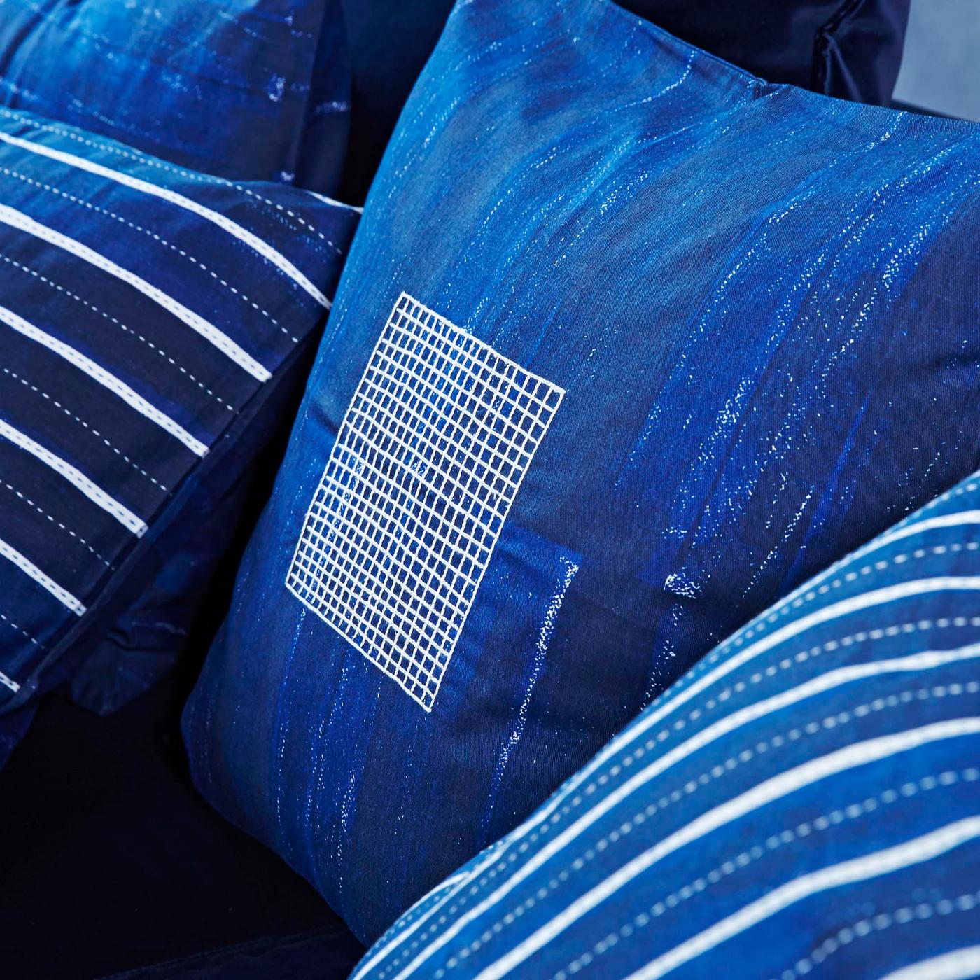 Three INNEHÅLLSRIK cushion covers in different shades of denim blue with white lines forming different graphic patterns.