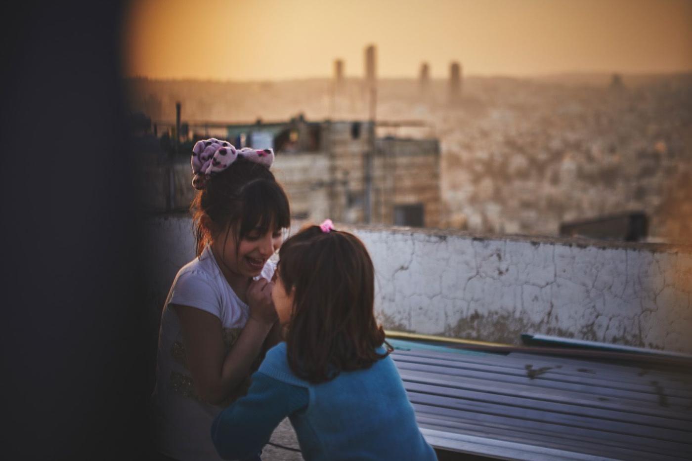 Two children playing on a rooftop overlooking a big city.