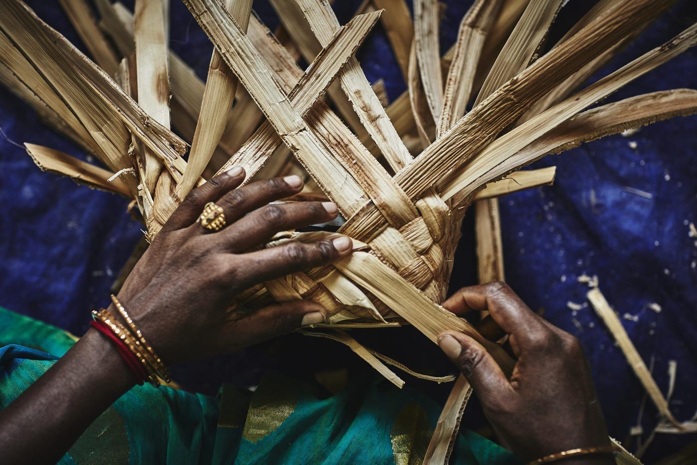 A pair of hands with gold bracelets crafting a banana-fibre basket.