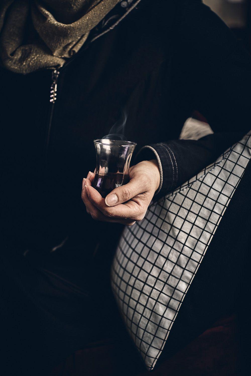 A person holding a glass of coffee leaning on a checked cushion.