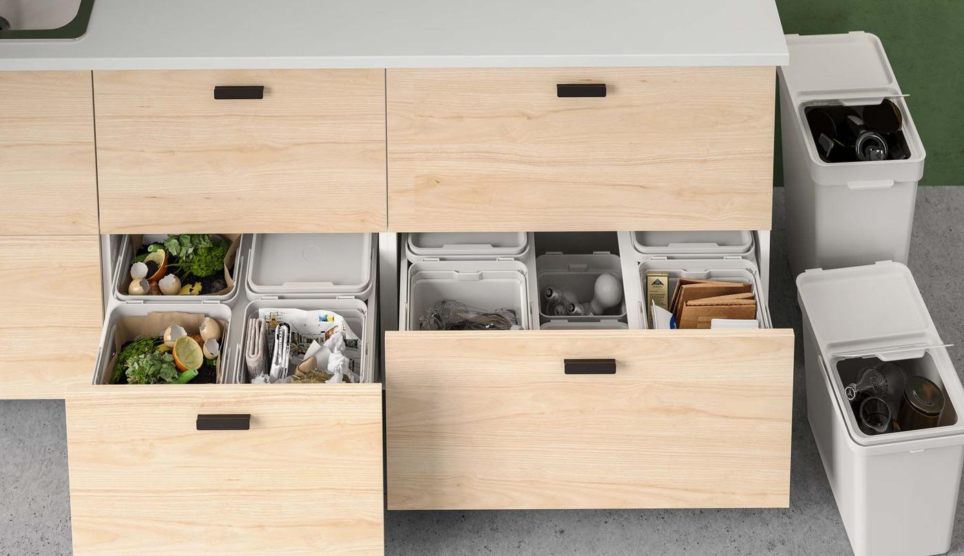 Two light wood drawers in a kitchen island unit are open, revealing a recycling system filled with newspaper, food waste and light bulbs.