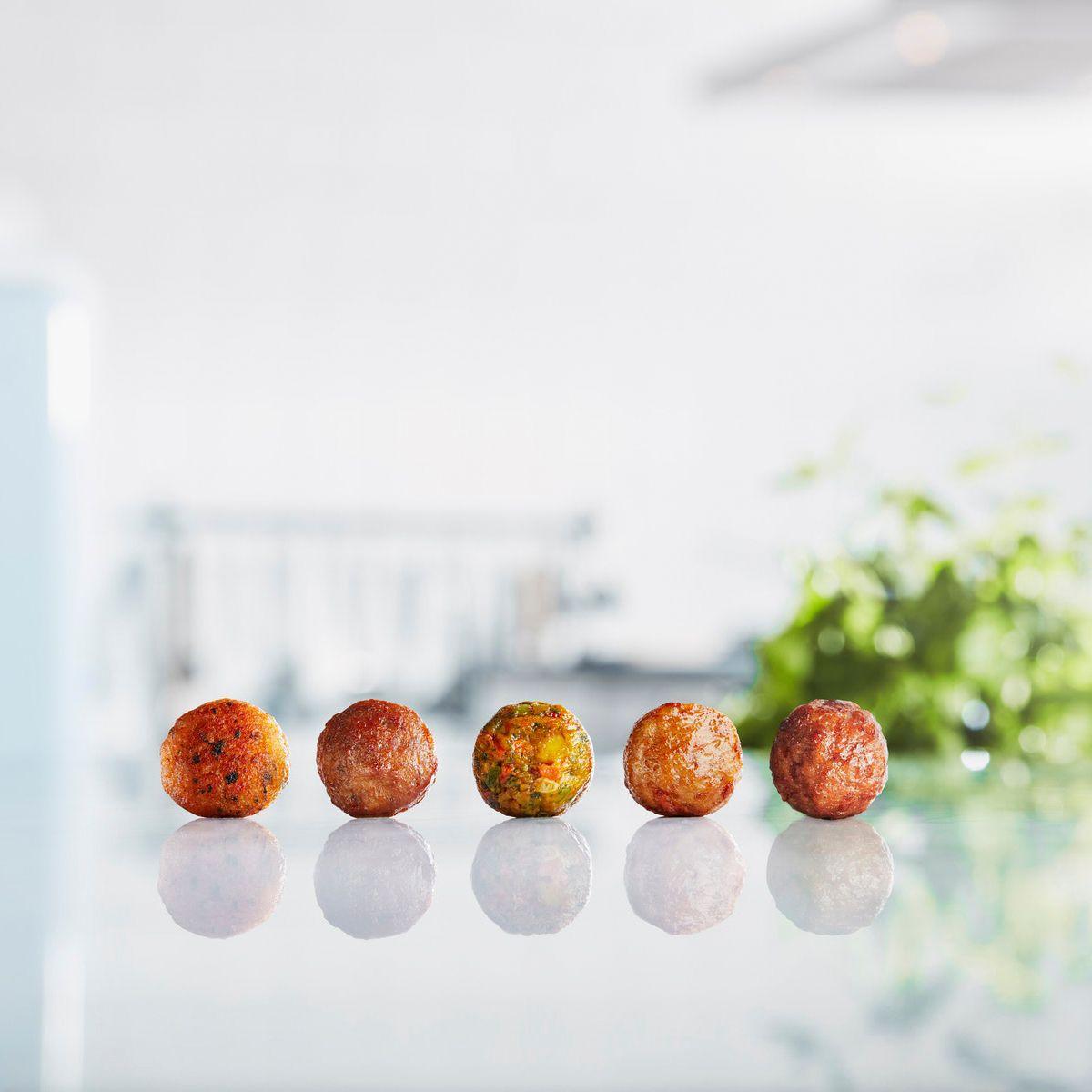Meatballs and plant balls in a row on a white surface, with green plants in the background.