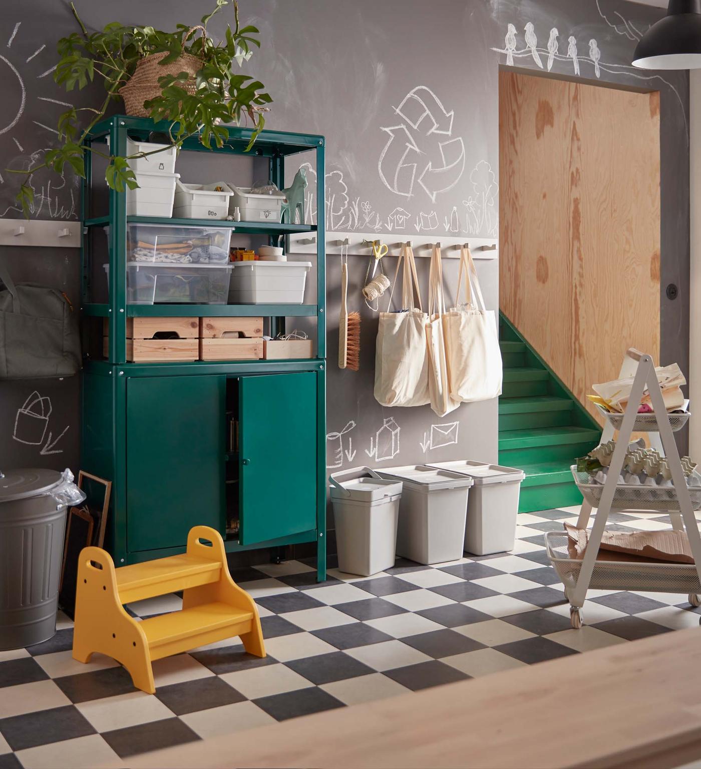 A hallwall with a chequerboard floor, green cupboards and three recycling containers lined up against the wall.