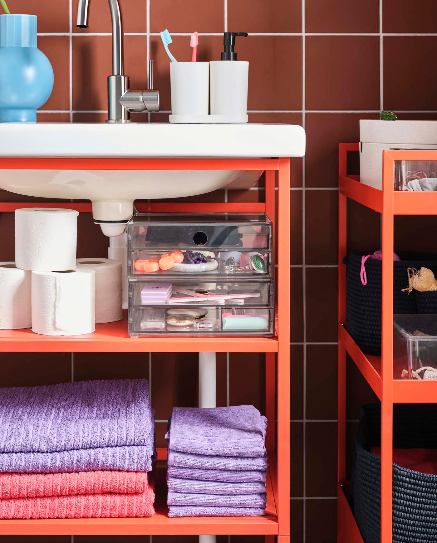 A red ENHET storage system next to a red NISSAFORS trolley in a tiled bathroom. 