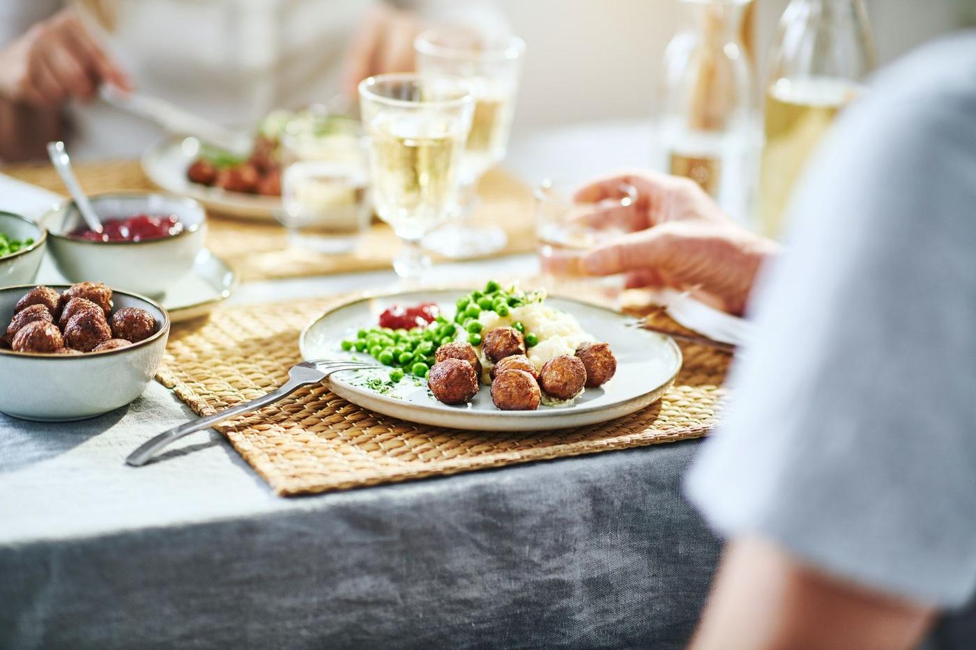 A dinner table with plates and people eating a classic meal of Swedish meatballs.