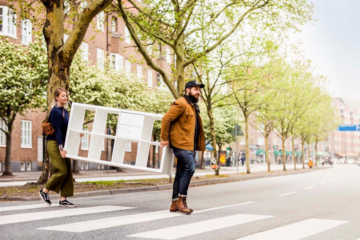 Two people crossing a street, carrying a white shelf.