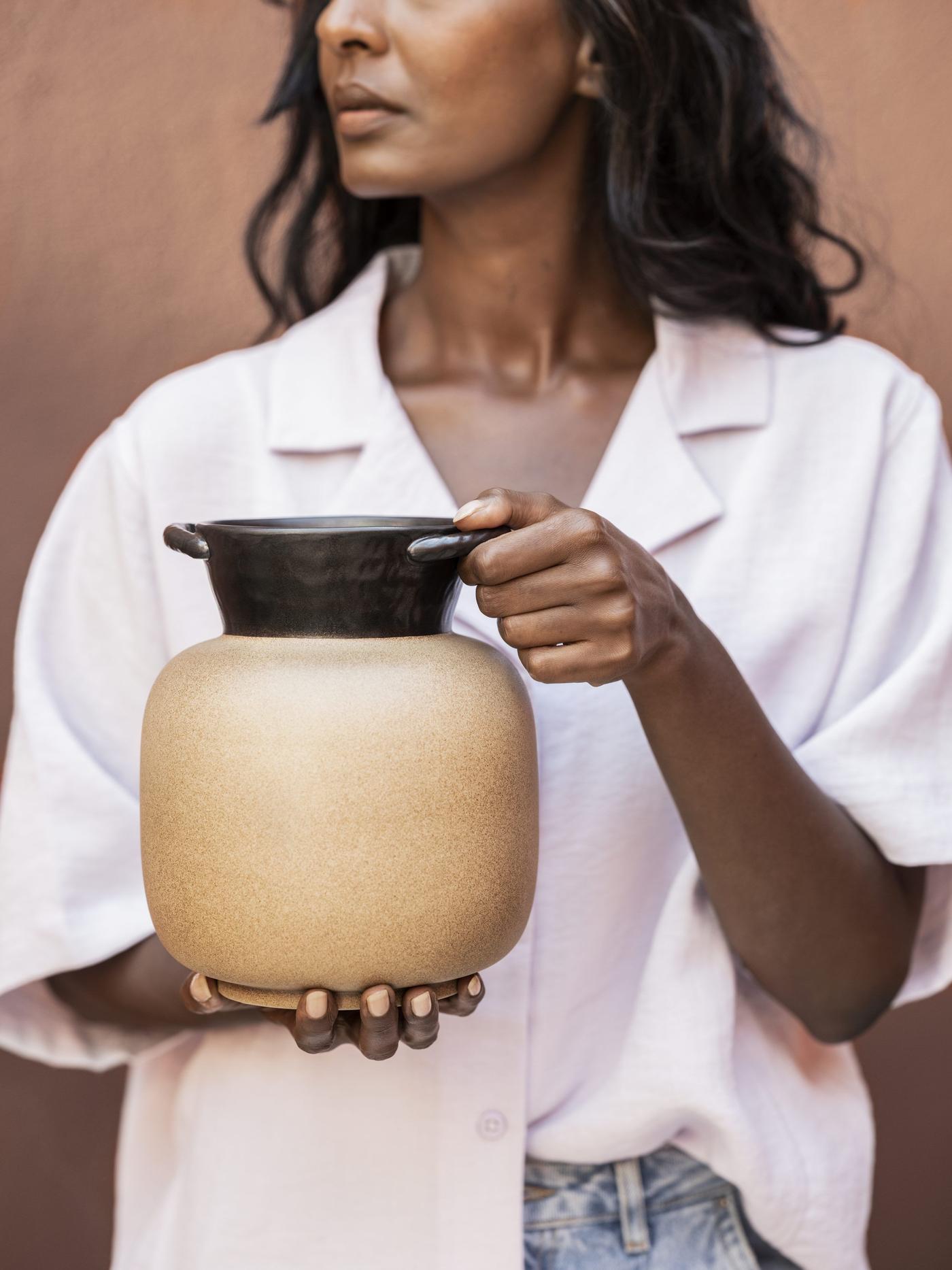 A woman in a white shirt holding a brown and black ceramic pot.