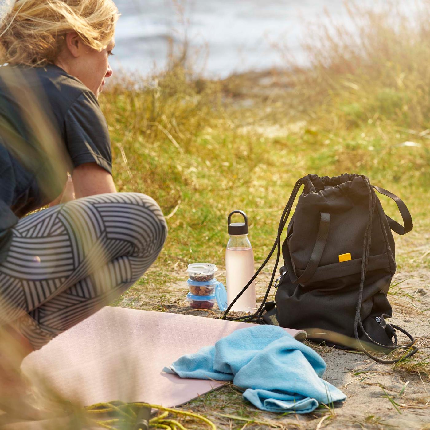 A grassy area with a person crouching next to a black VÄRLDENS gym bag and a light blue KORNAN hand towel.