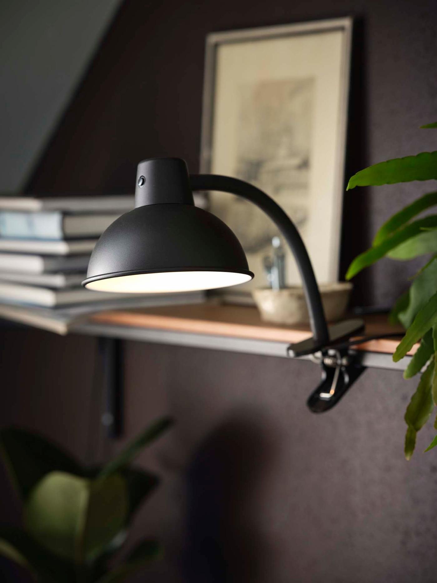 A lit industrial-style black lamp clamped to a shelf on a dark grey wall.