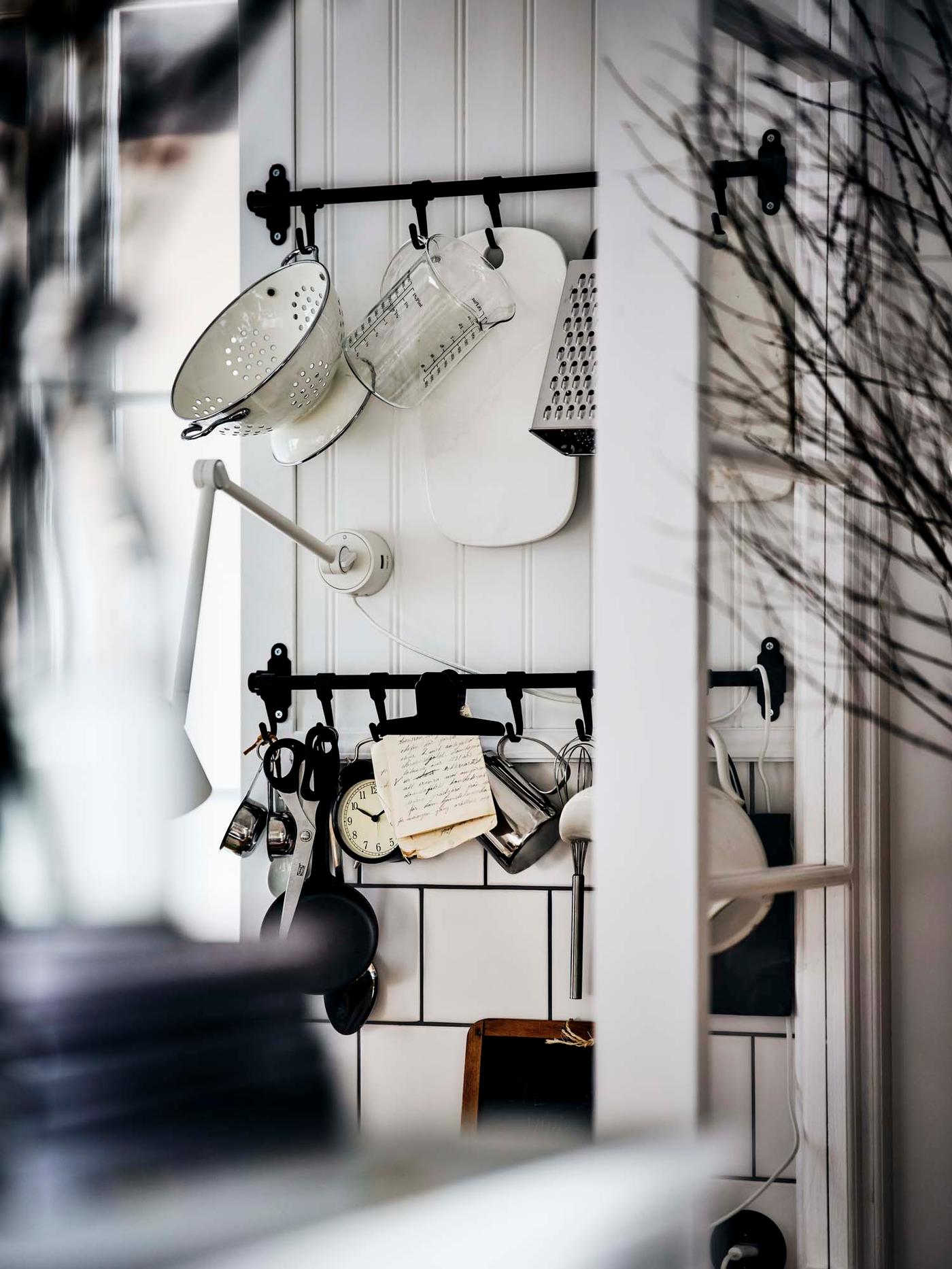 A traditional black HULTARP rail with hooks is used to store cooking utensils in a white kitchen.