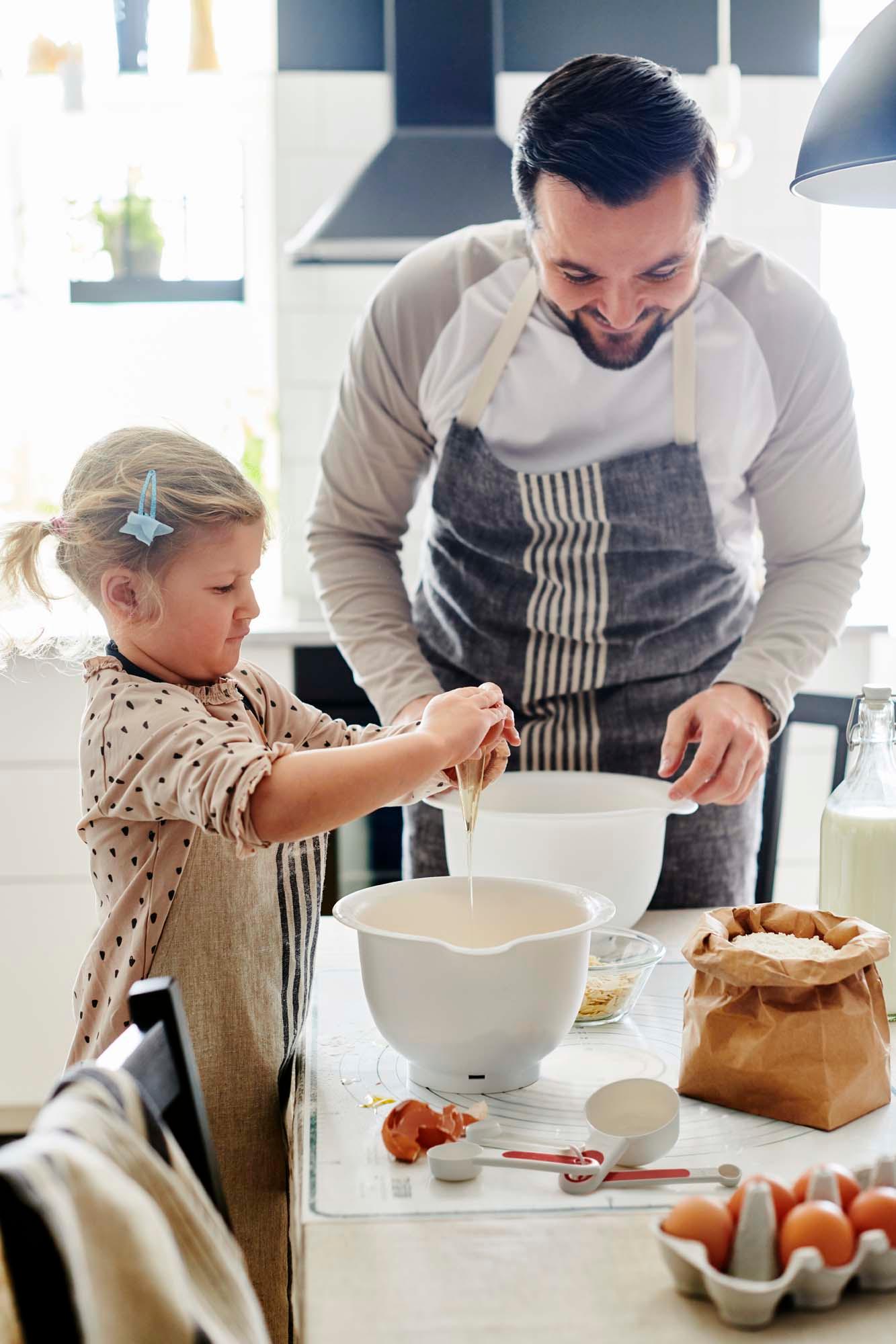 A parent and child baking together in a black and white kitchen.