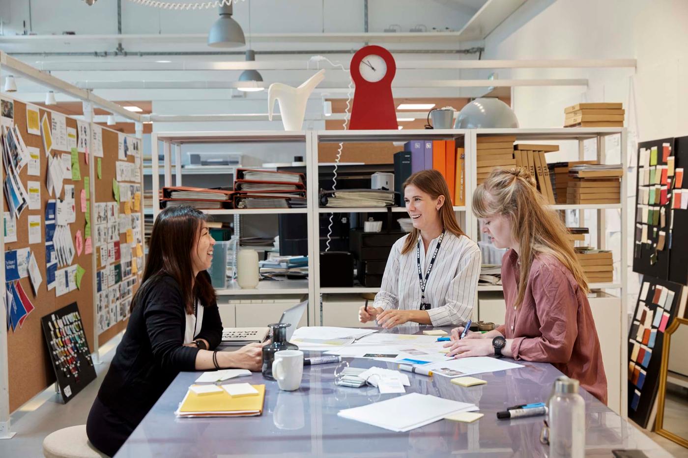 Three people chat while sat round a work desk in the offices of IKEA of Sweden.