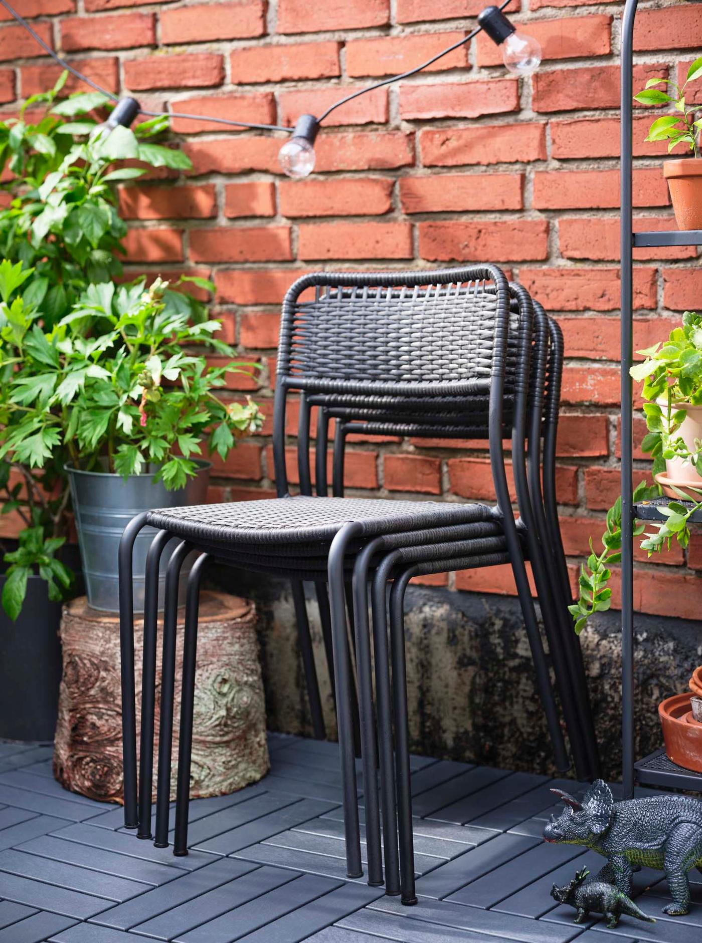 Four stacked outdoor dark grey VIHOLMEN chairs in an outdoor space.