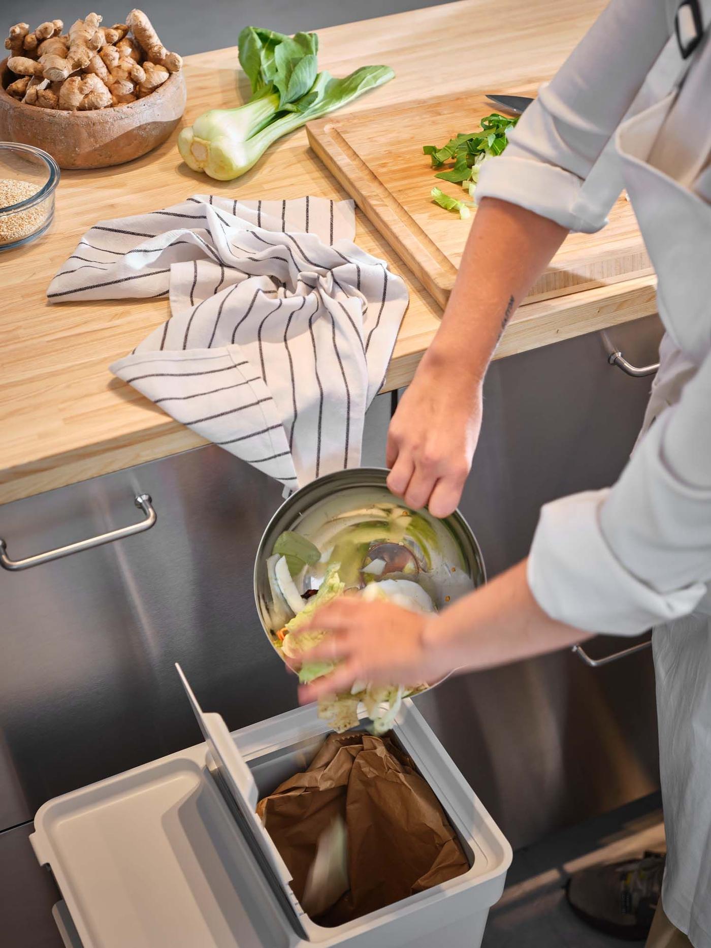 A person scrapes organic waste into an under counter recycling container.
