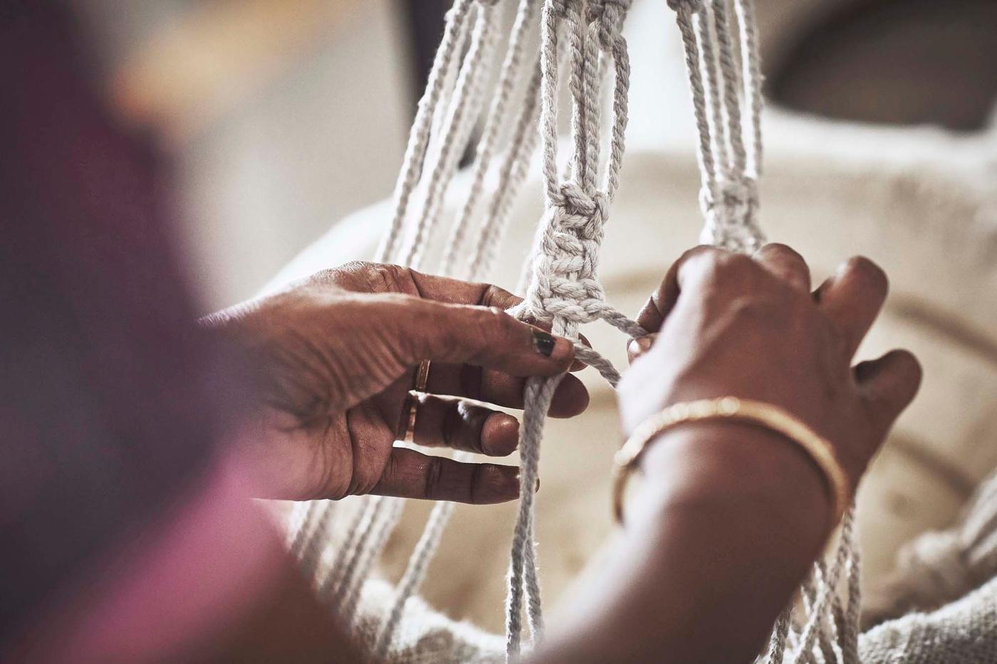 A person knots natural fibres to create a decorative home item.