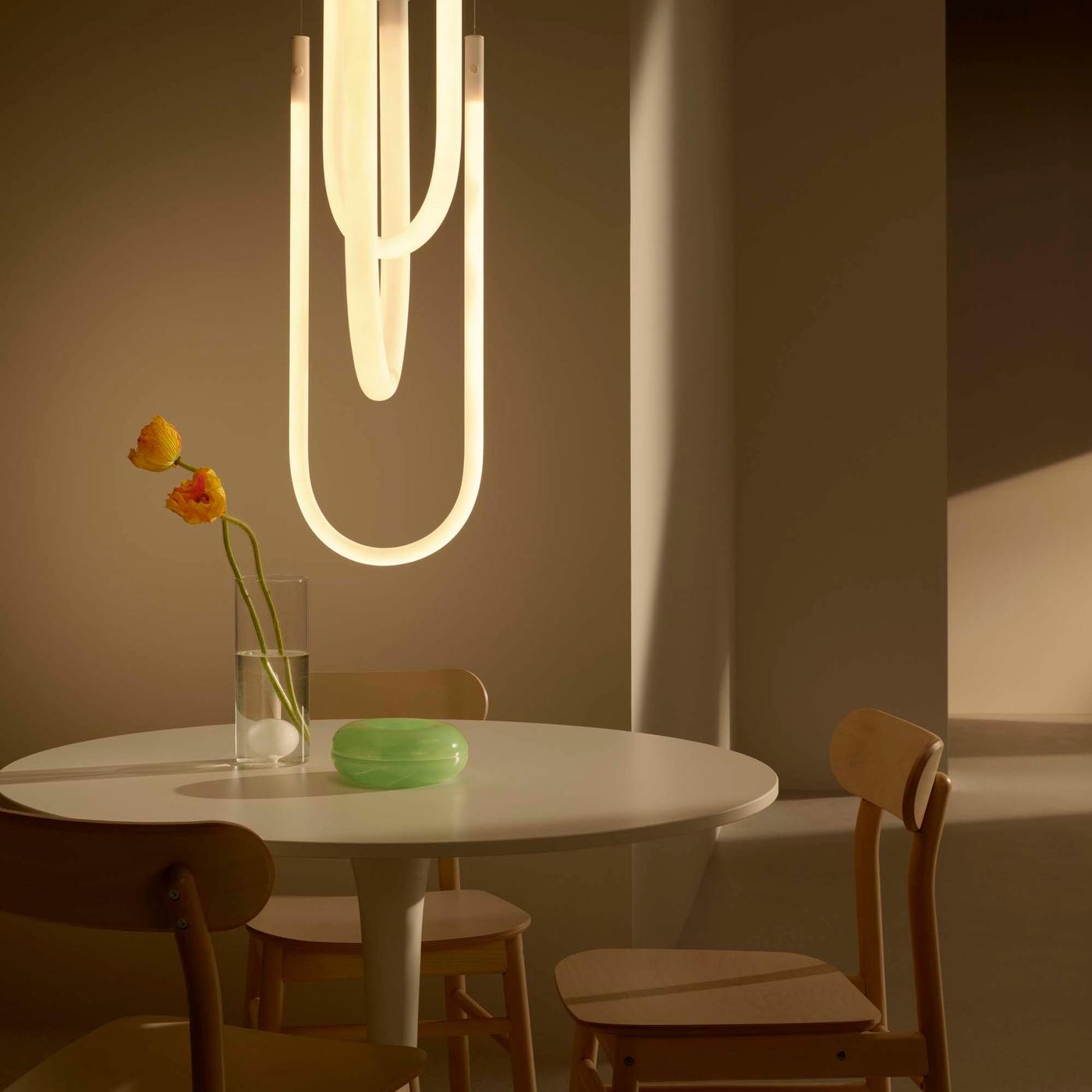 A glowing sculptural ceiling light hangs over a white round dining table.