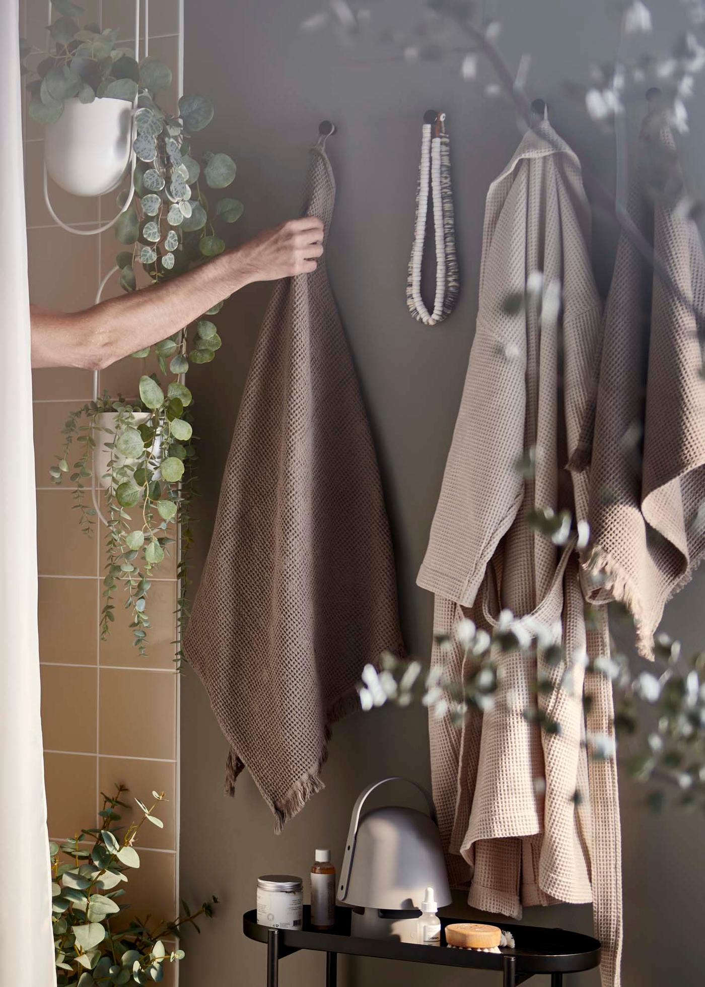A hand reaches out of the shower to grab a towel from a hook on a grey wall.
