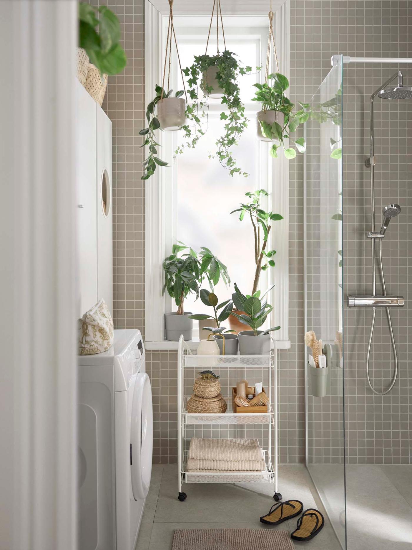 A small bathroom with grey tiled walls. To the left is the laundry area and to the right a shower, with a trolley in the centre.
