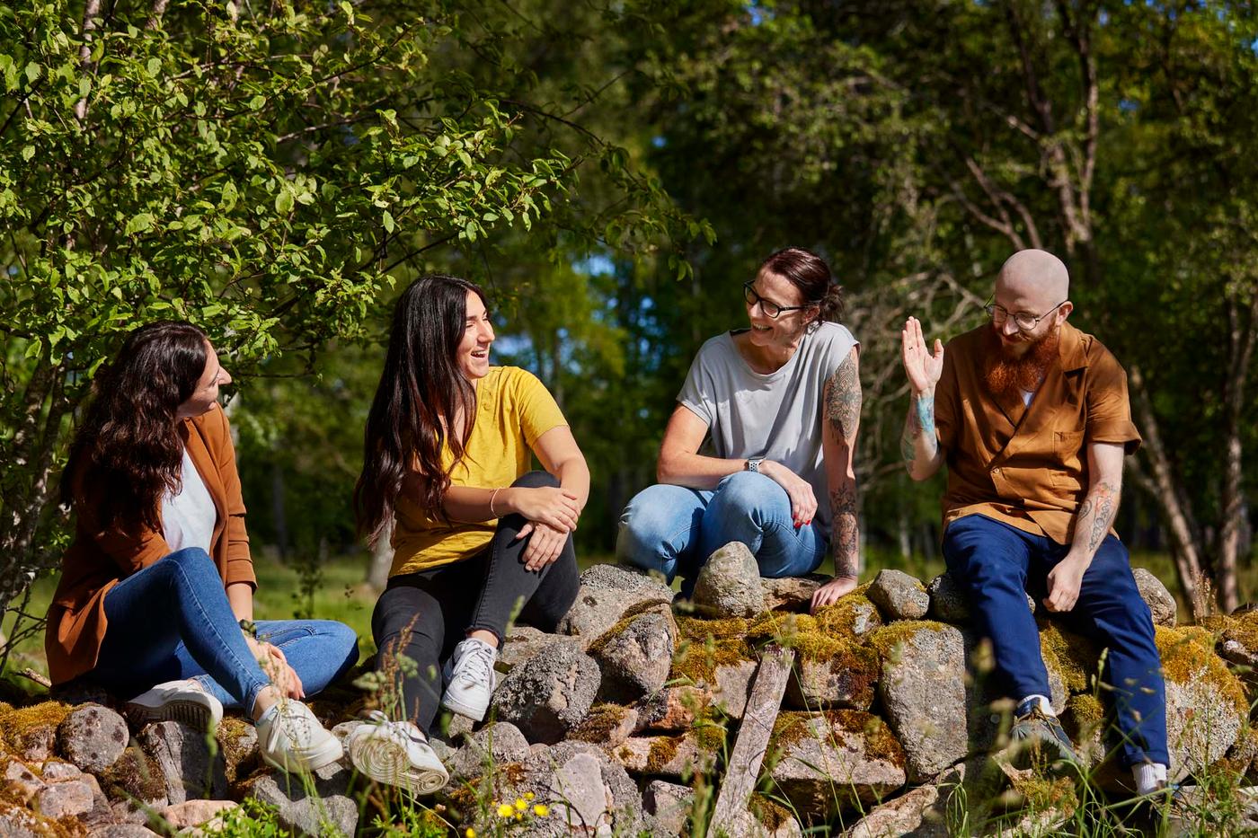 Four co-workers laughing together while they sit in the sun on an old stone wall with the forest behind them.