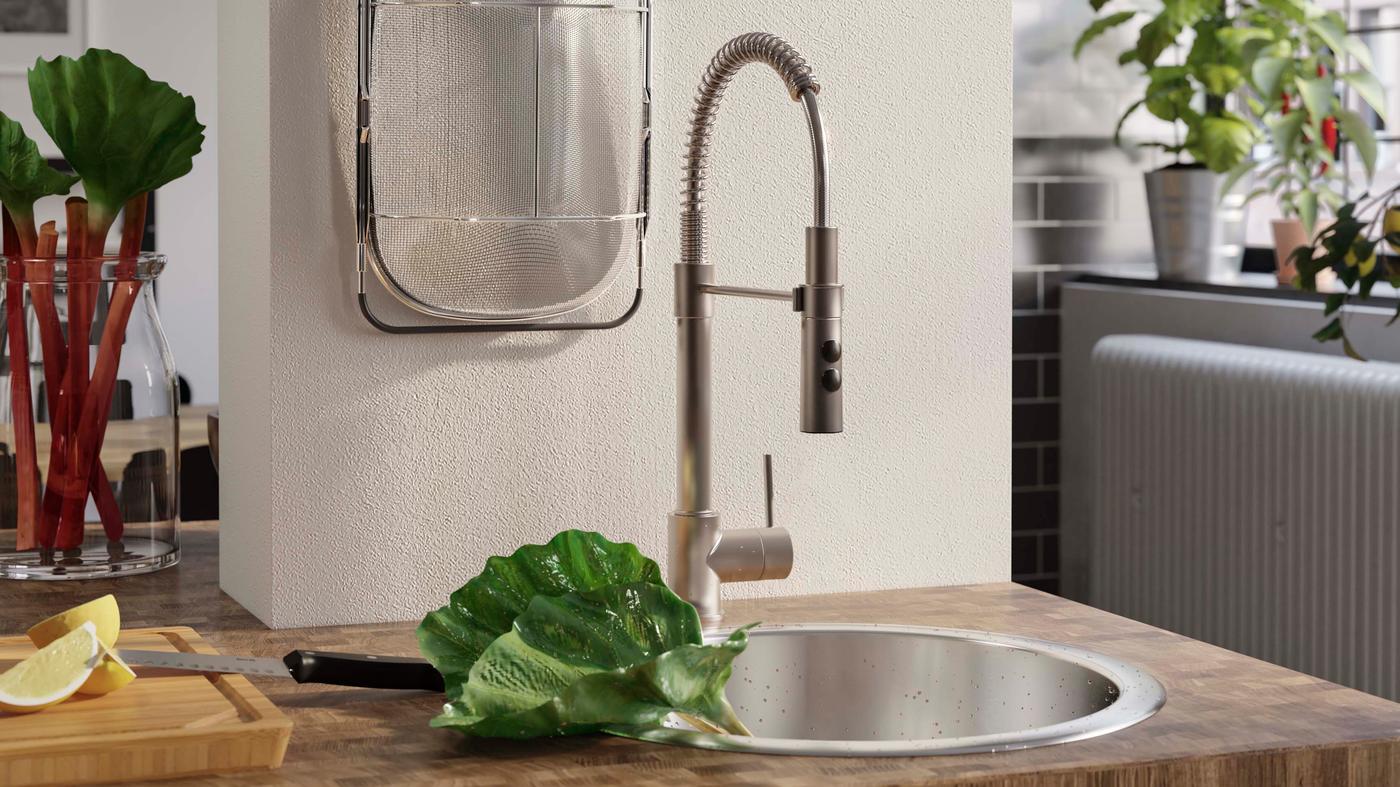 A close-up of the VIMMERN tap with hand spray in stainless steel in a white and wood. kitchen.