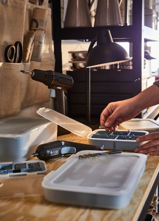 A person's hand taking a screw from a plastic container on a workshop surface.