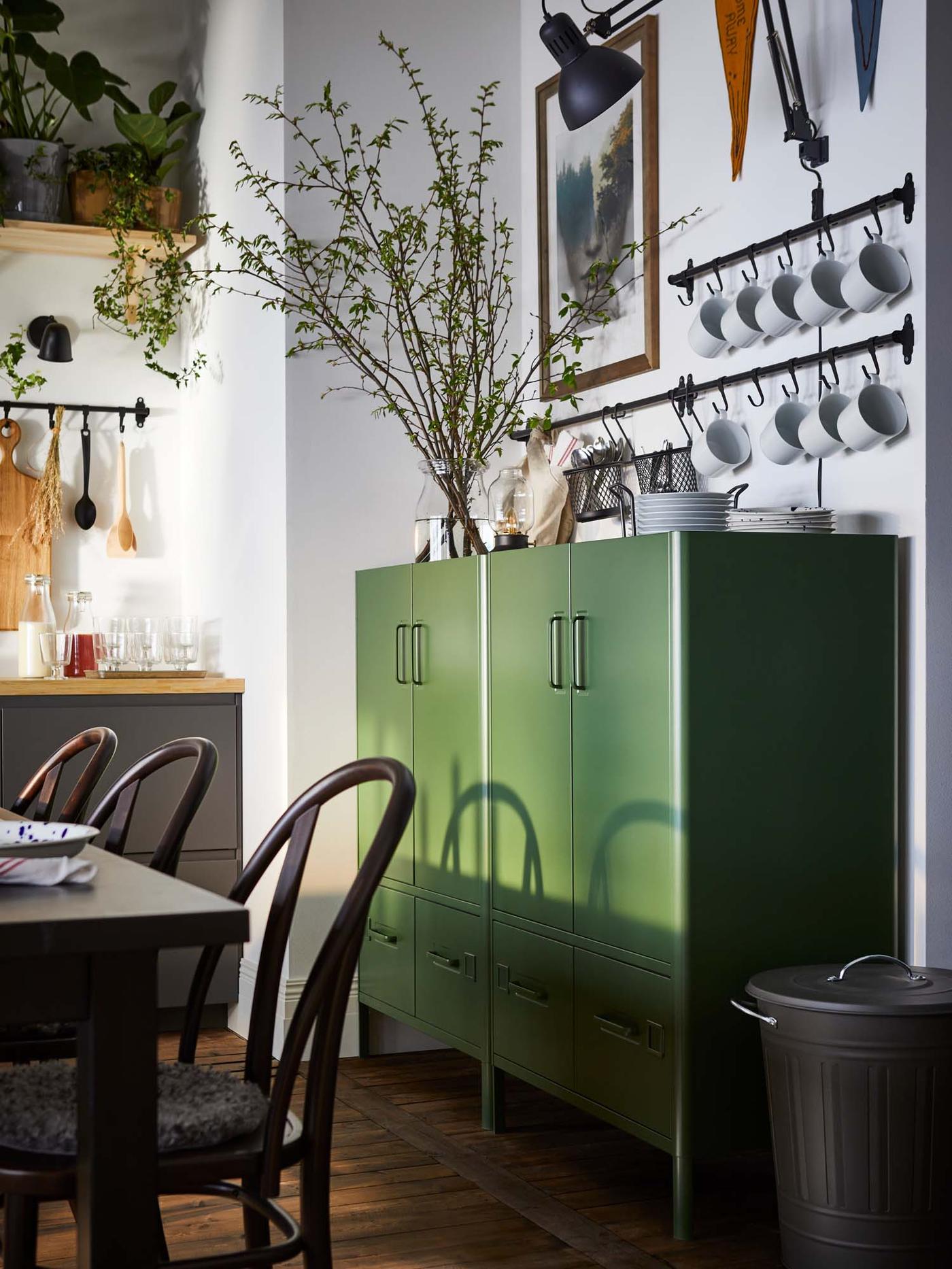 A dark grey KNODD bin stands next to a dark green storage unit in the dining room.