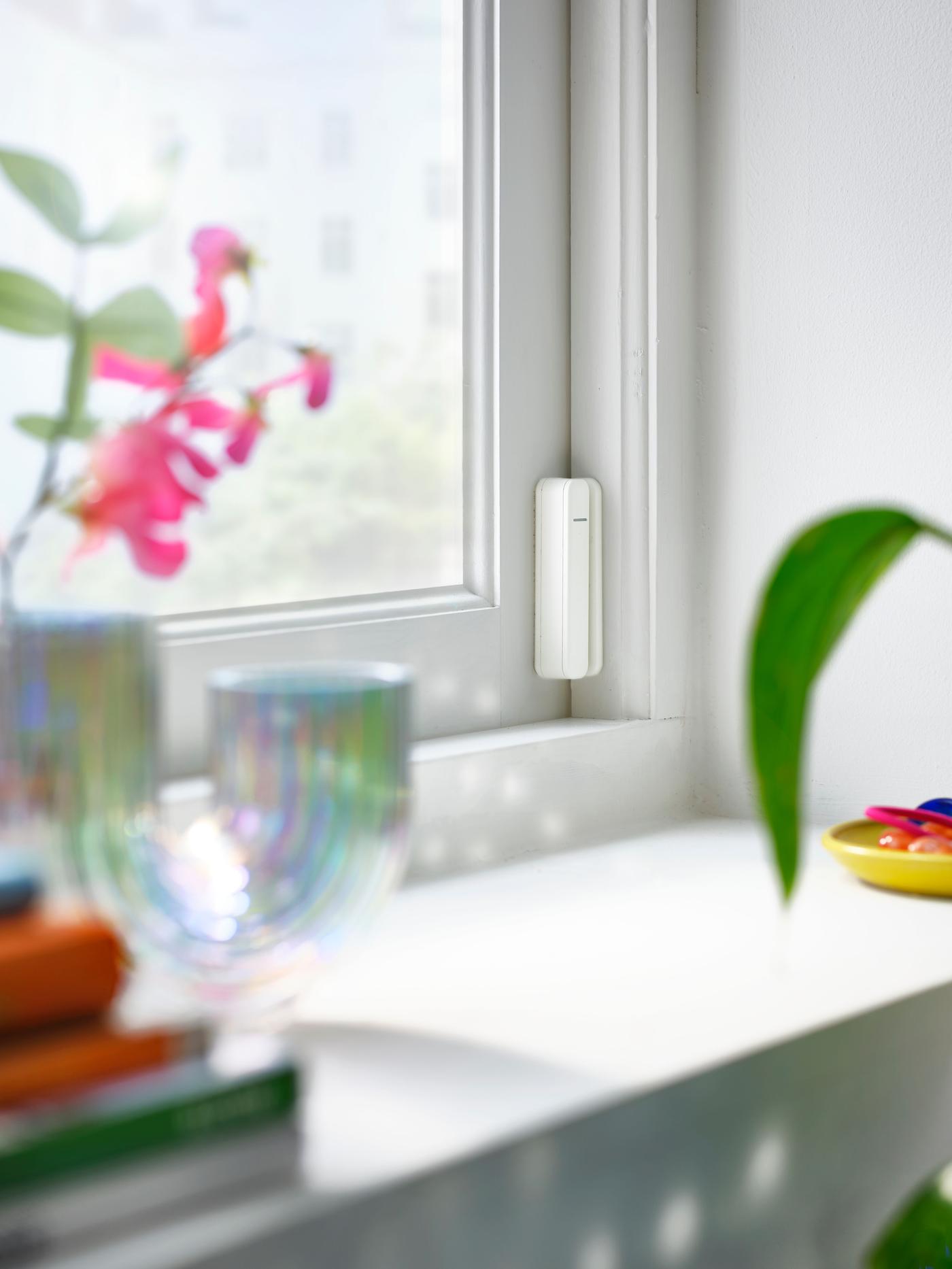 A white sensor placed on the side of a window, with flowers in the foreground.