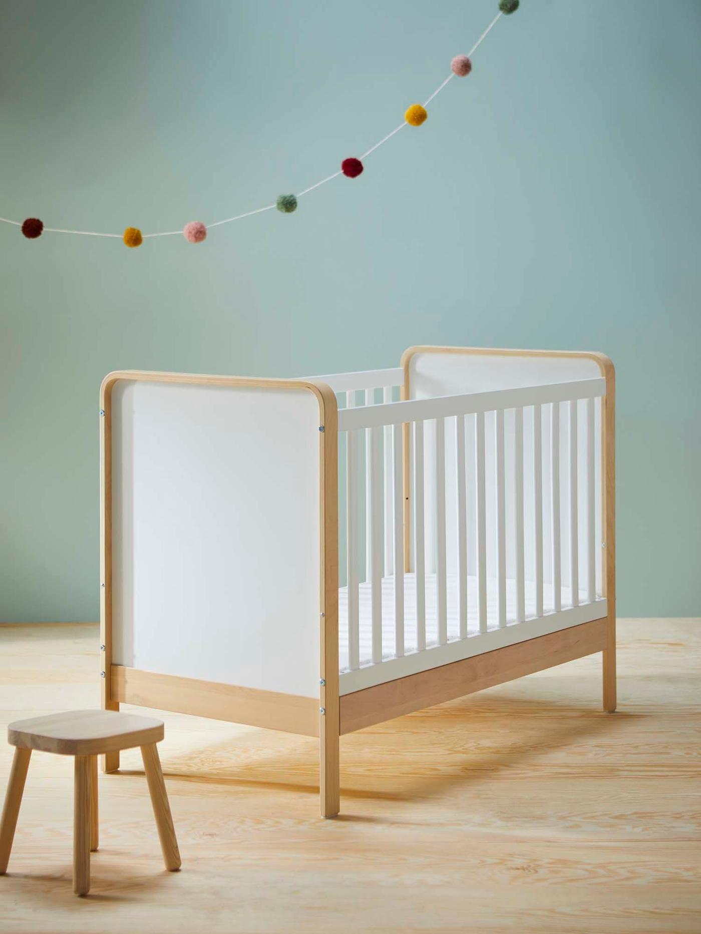 A white cot against a blue backdrop and light wood floor with a decoration hanging above.
