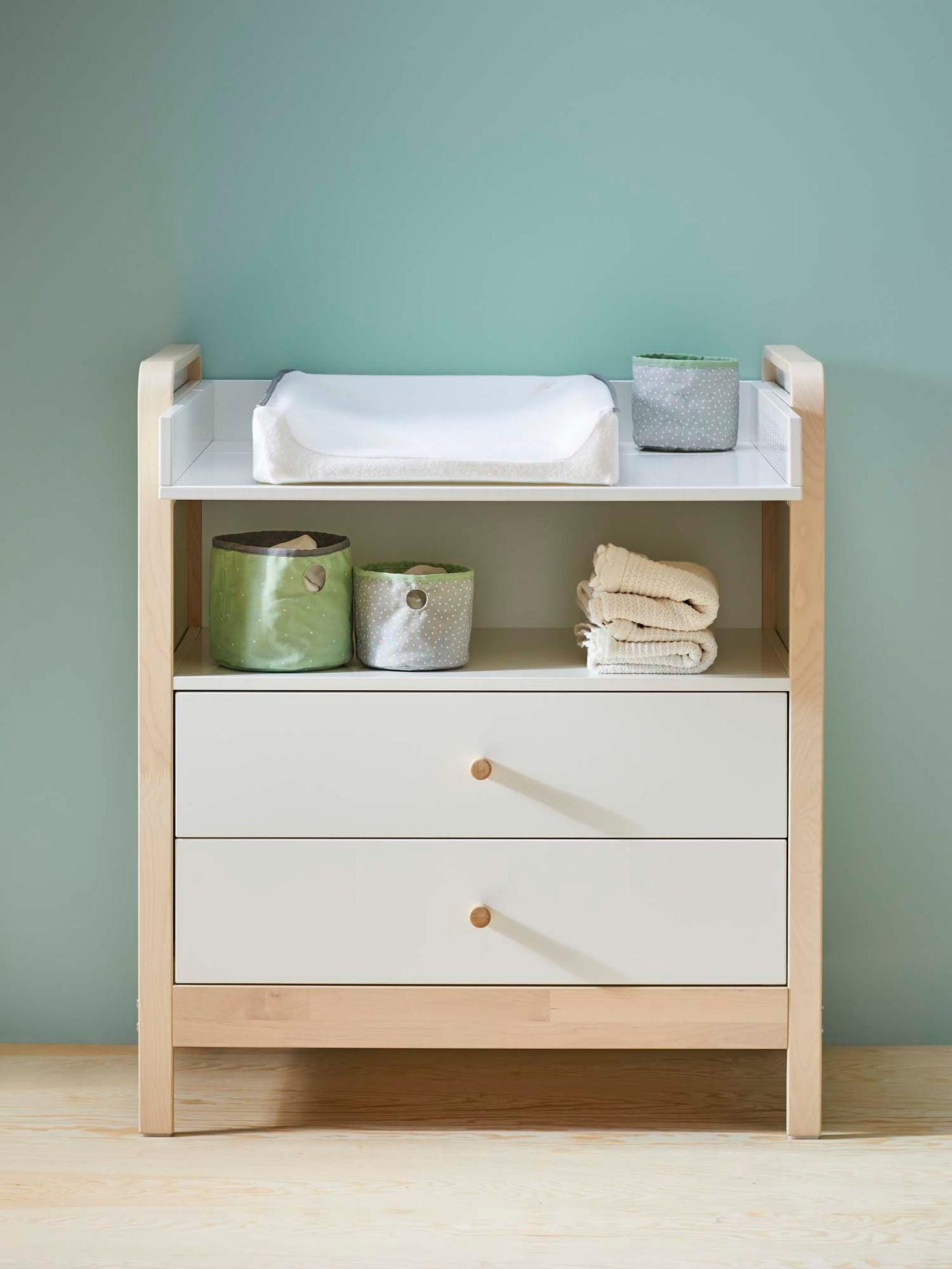 A changing table/chest of drawers with a mat and changing supplies, against a blue background and light wood floor.