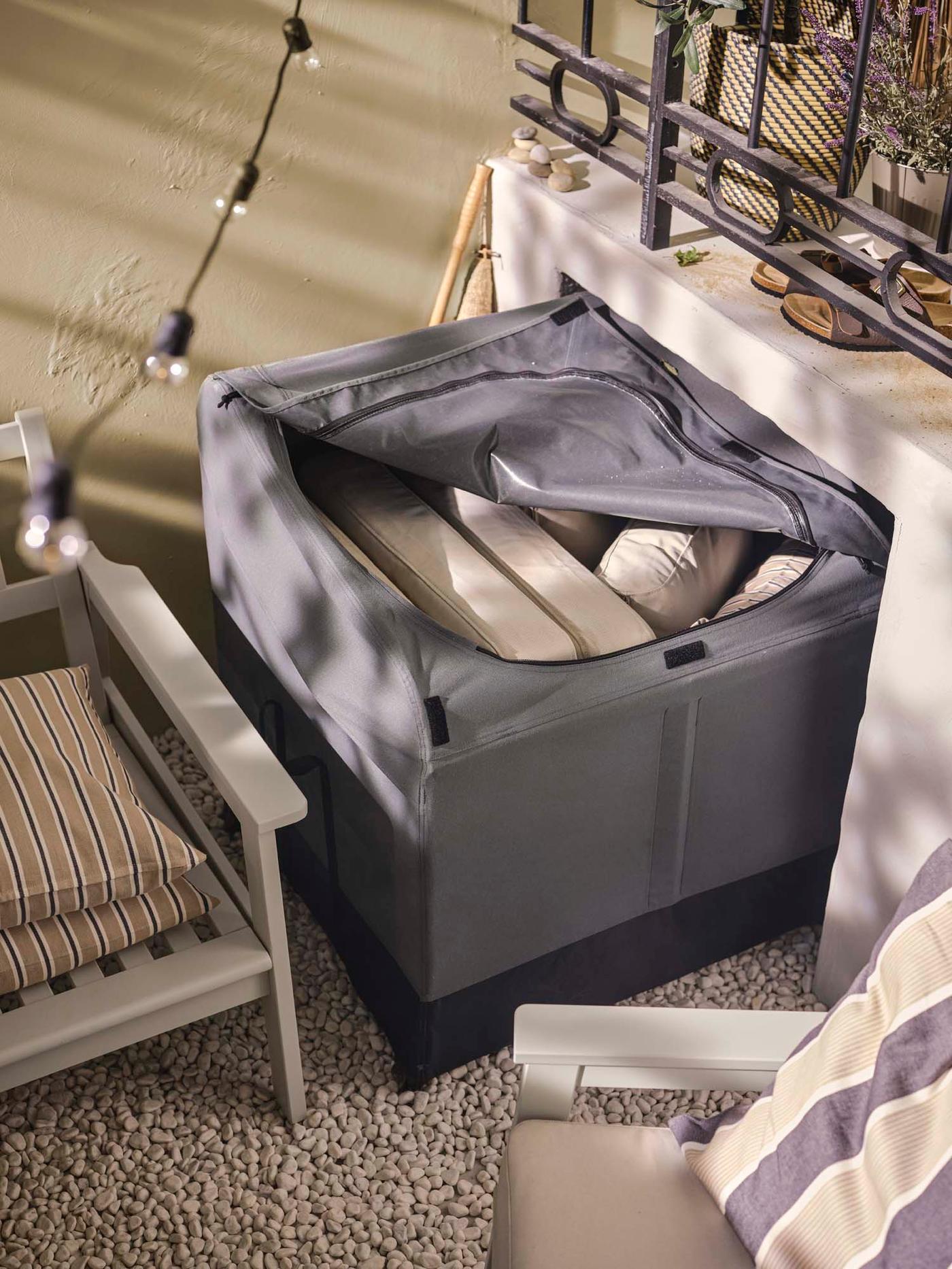 An outdoor area with a partially open VÄTTERSÖ storage box, revealing cushions inside.