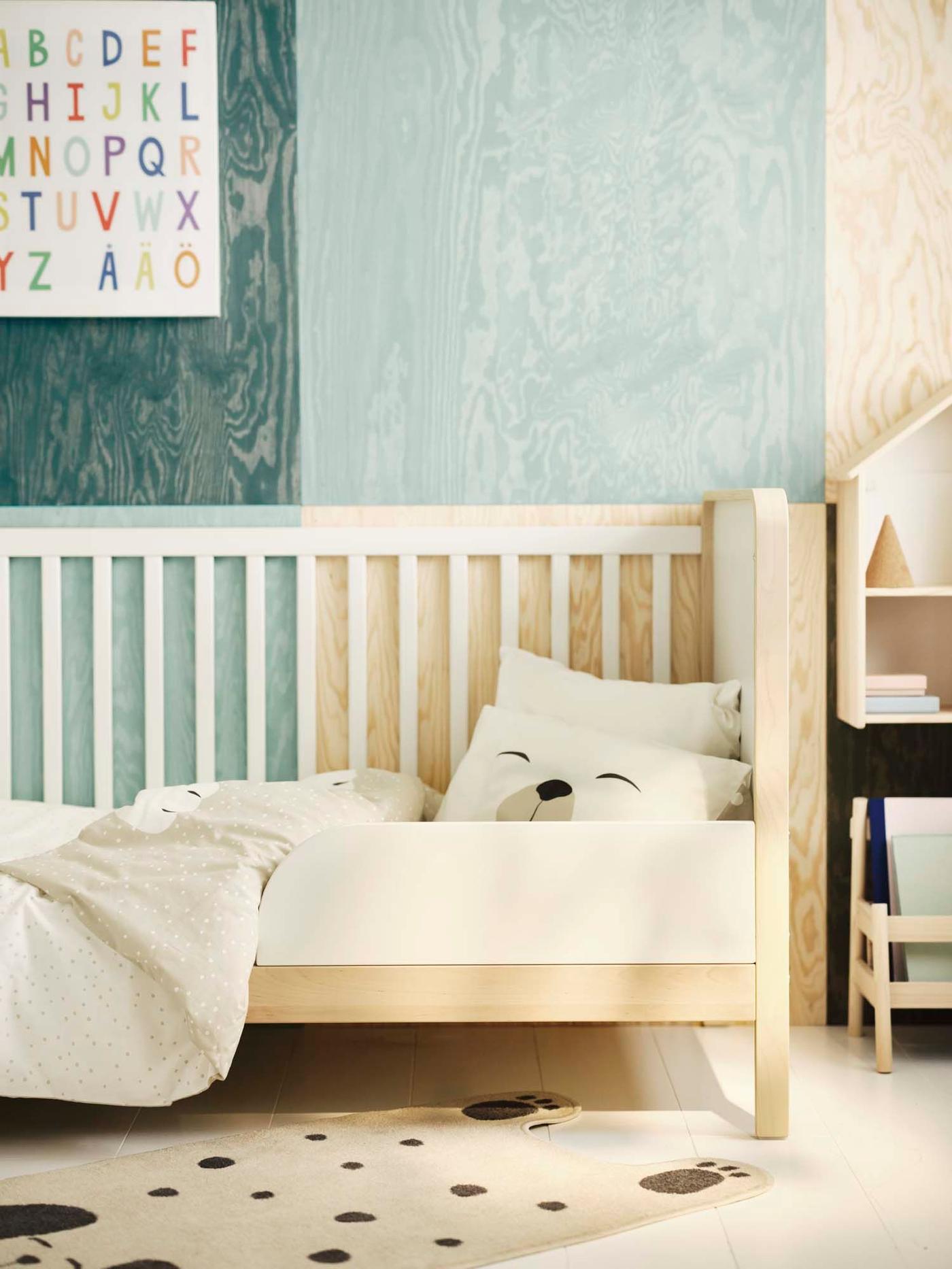 An open cot with a bear pillow in a blue and light wood nursery.