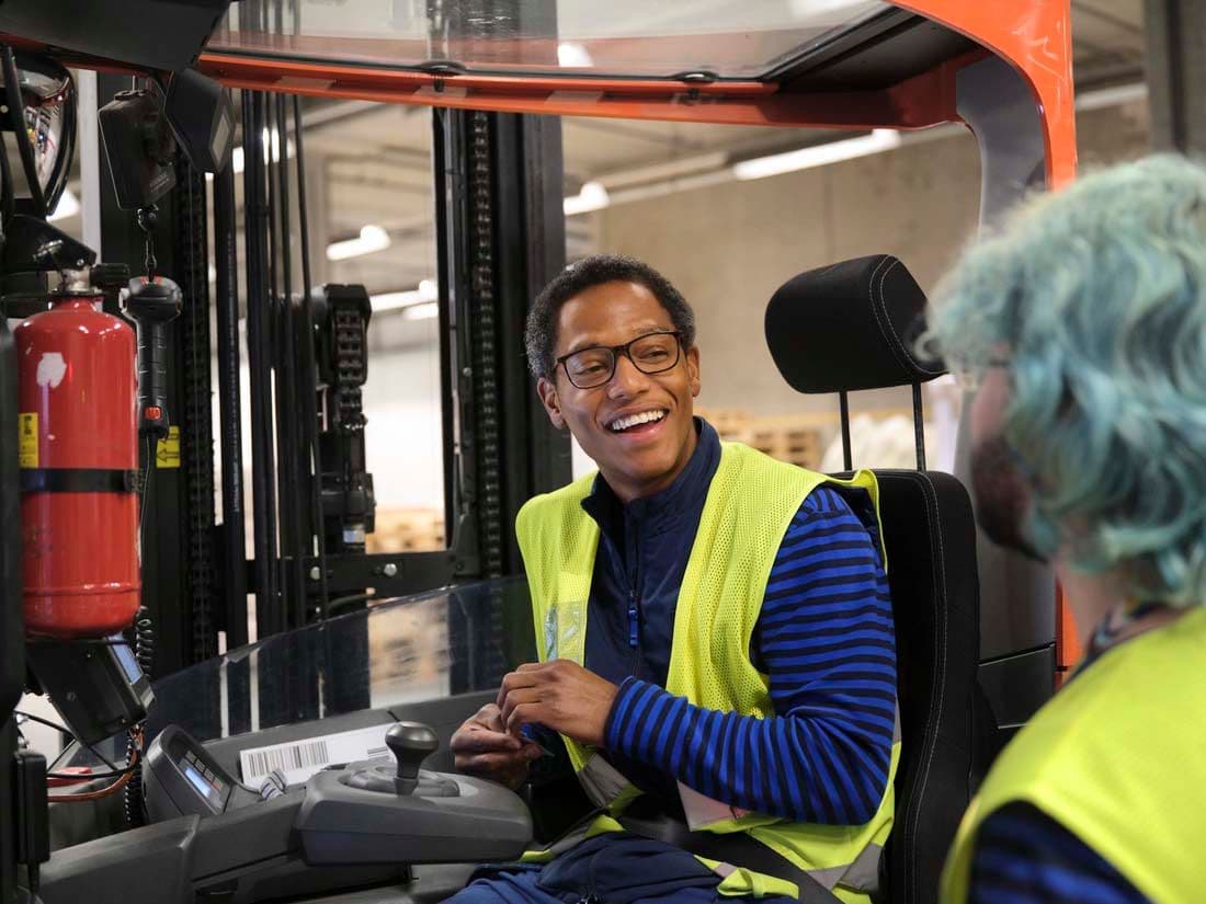 A factory worker chats to a colleague while sat in a forklift.
