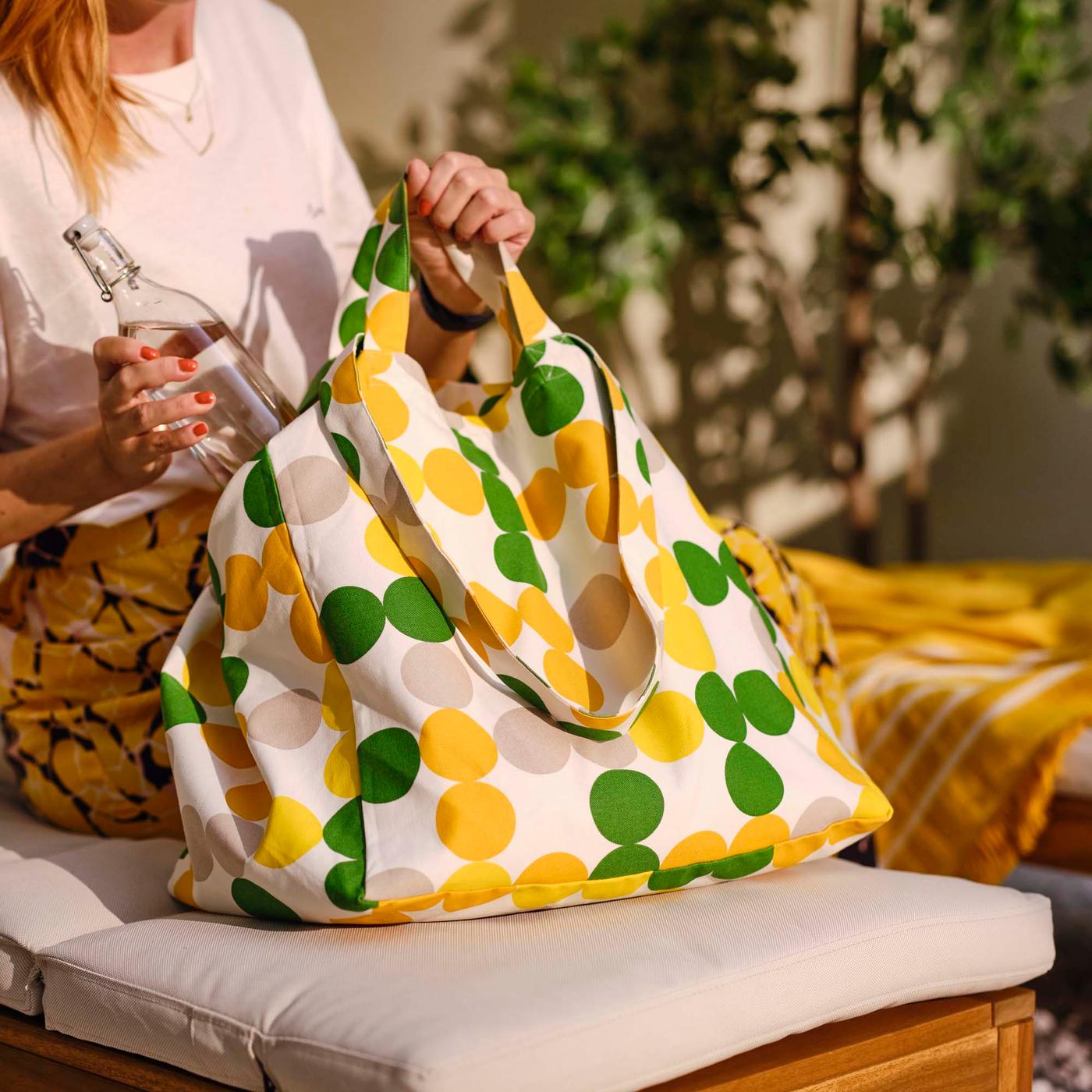 A person putting a drinking bottle into a dot pattern multicolour BRÖGGAN beach bag.