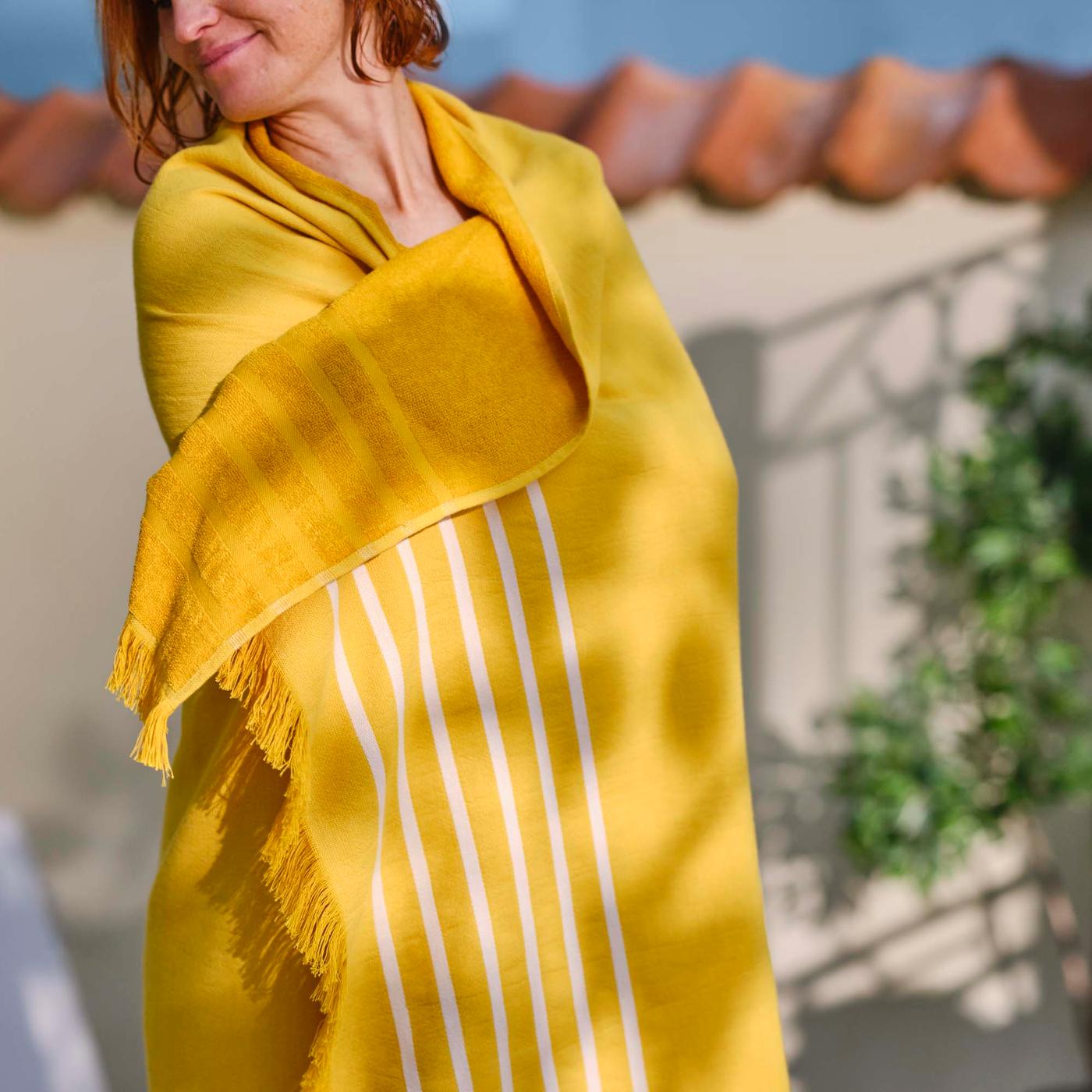 An outdoor space with a person wrapped in a BRÖGGAN beach sheet.