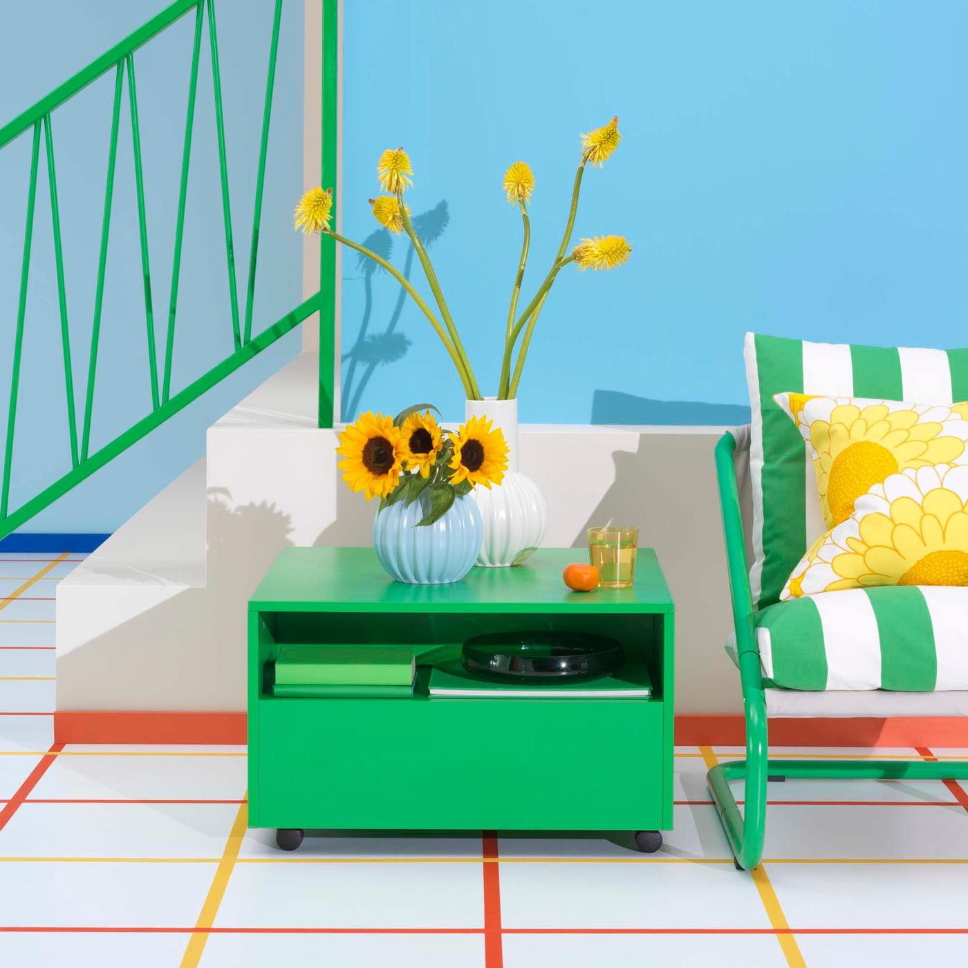 A bright green GARNANÄS coffee table with a vase on top sits next to a striped chair, in front of a blue wall.